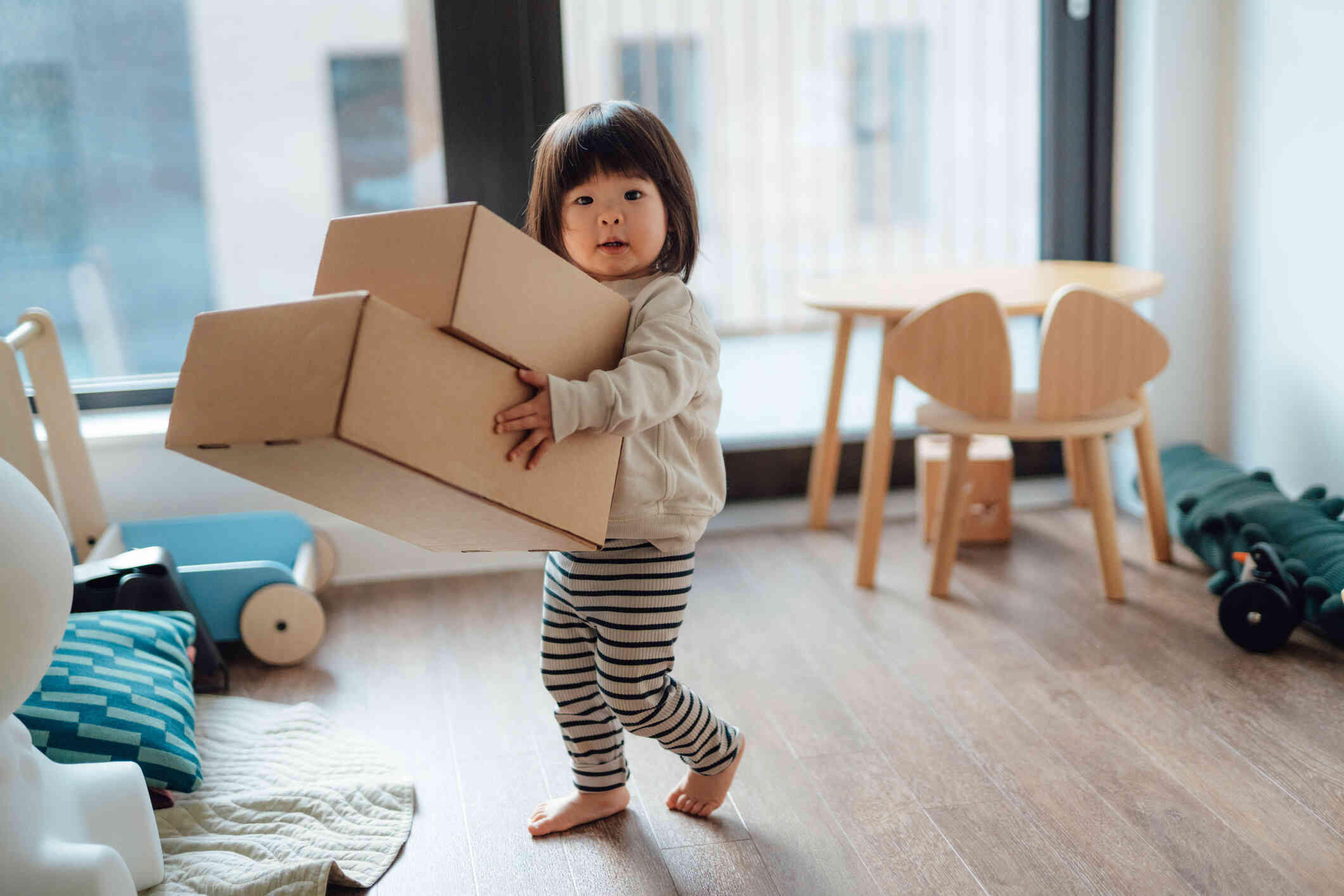 A young curl carries two cardboard boxes through the living room quickly while glacing at the camera.