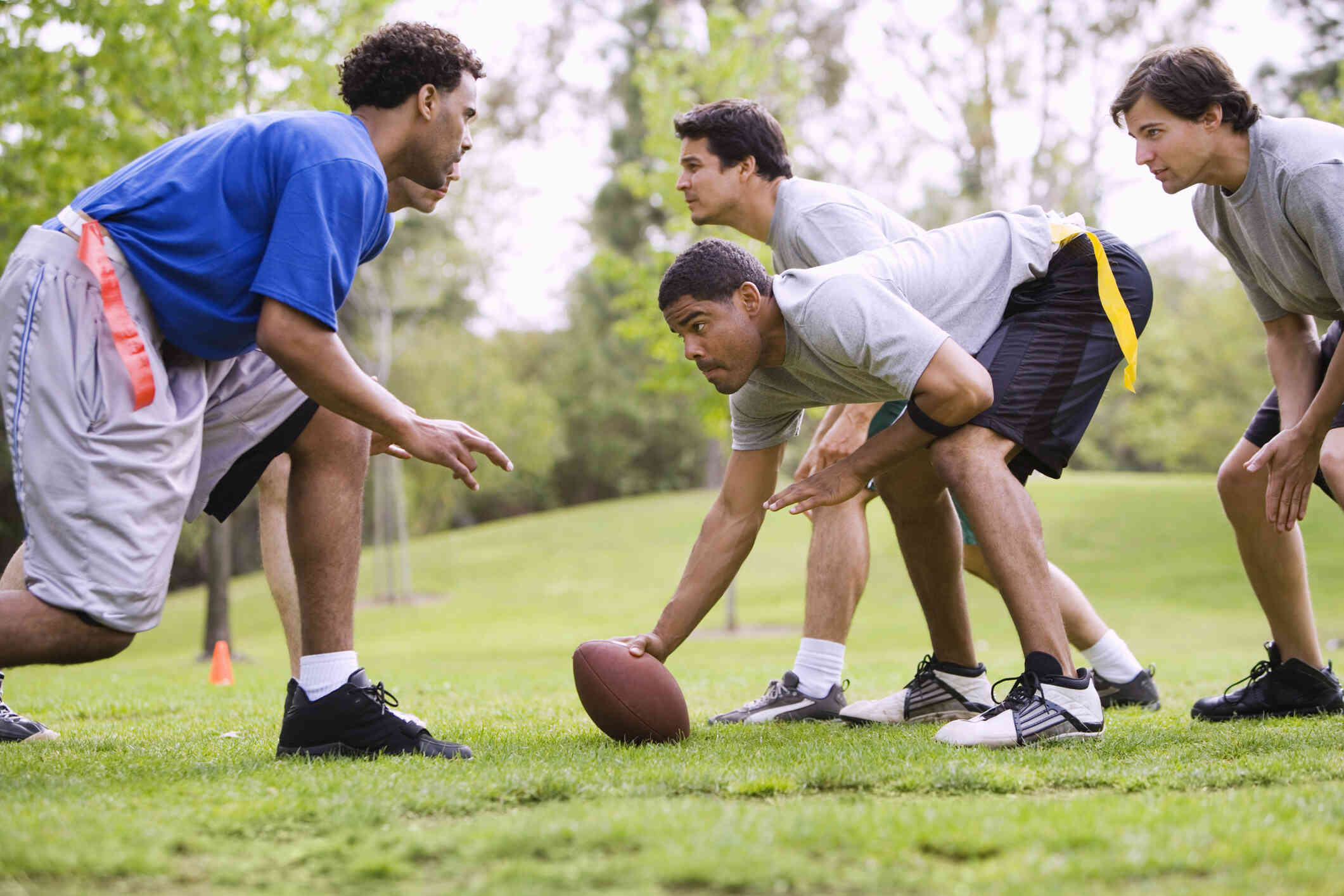 A group of male friends play football together in a grassy field on a sunny day.