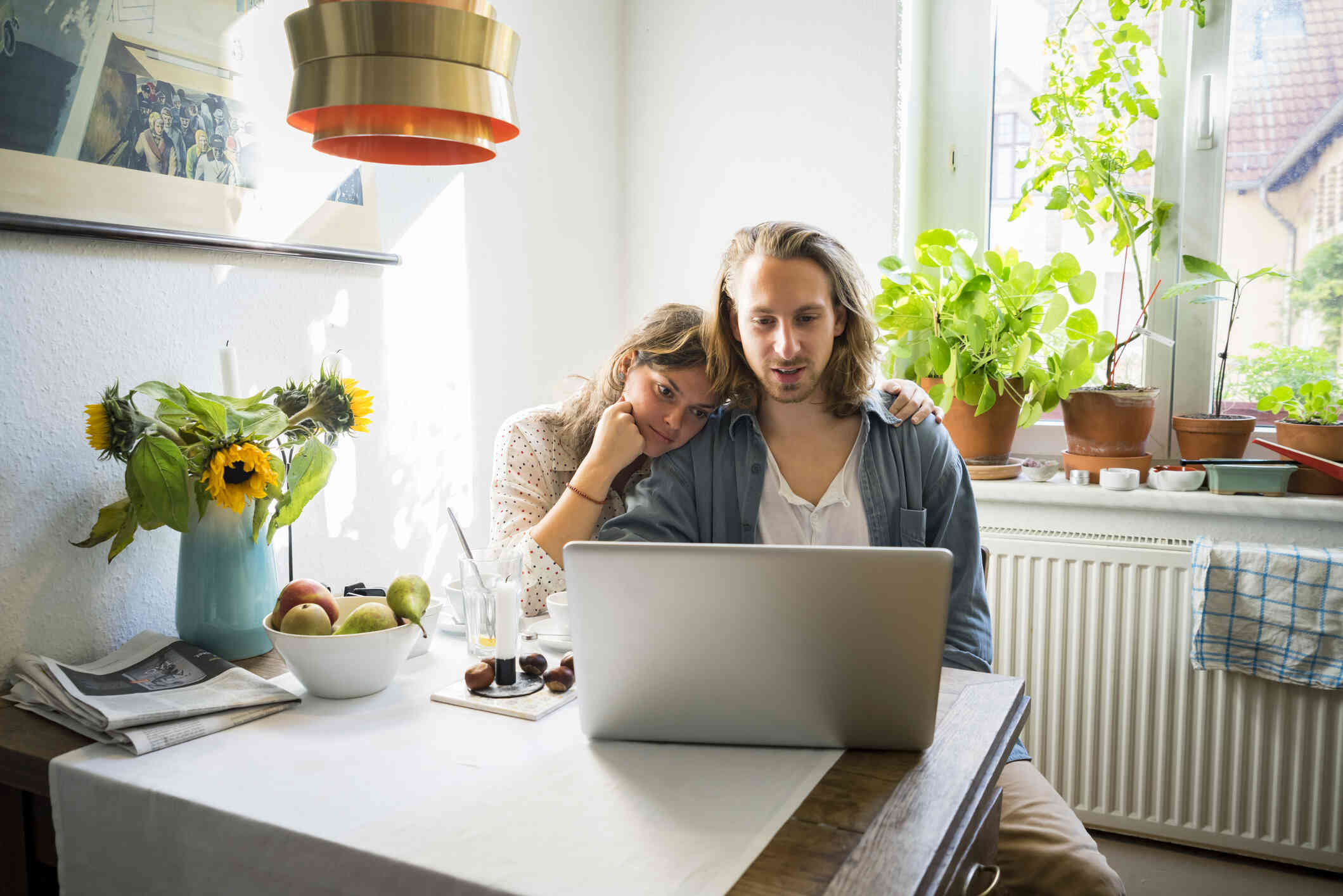 A couple seated at their dining table, both focused on using the laptop.