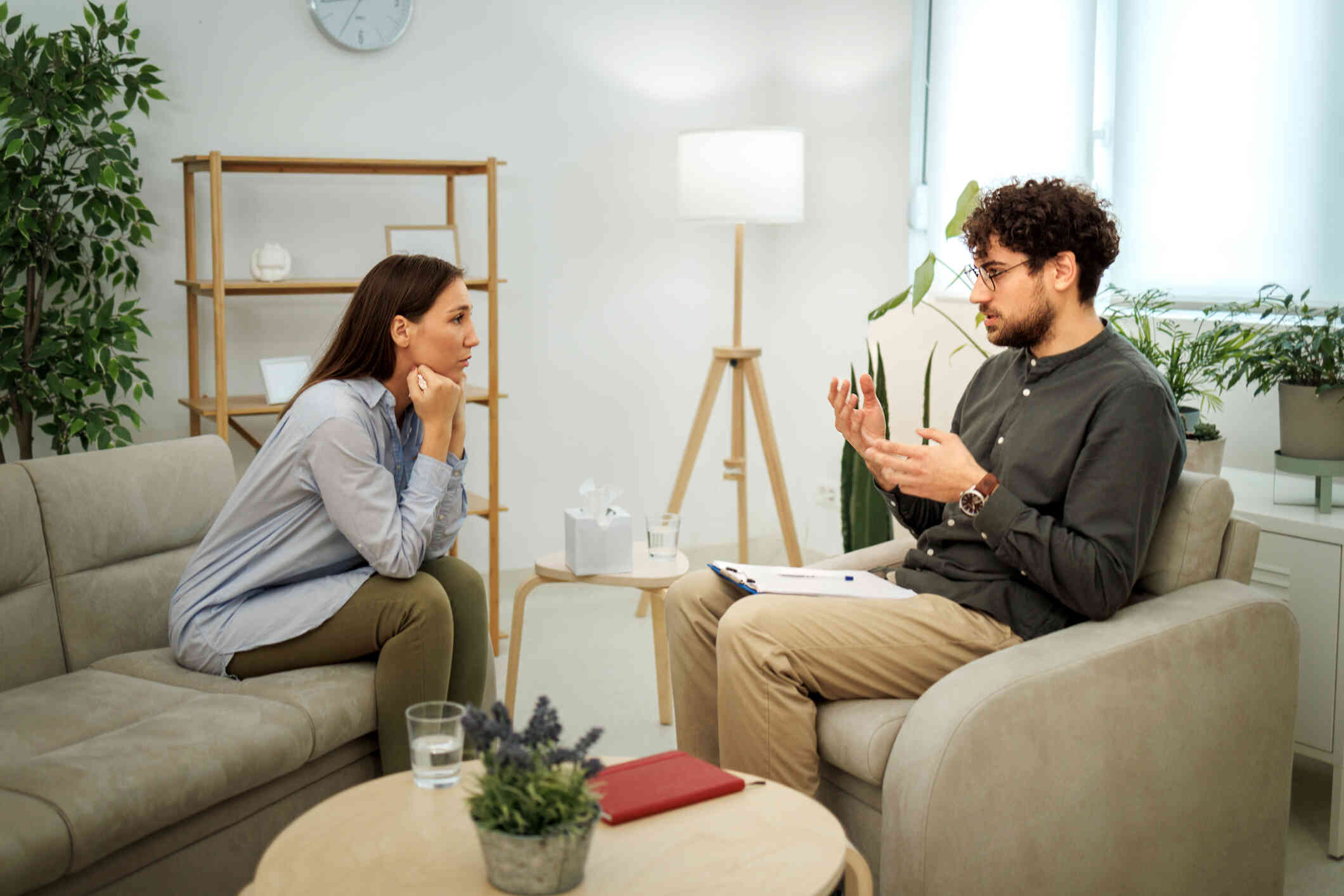 A woman leans forward on the couch in her therapists office and listens intently as her male therapist talks during a therapy session.
