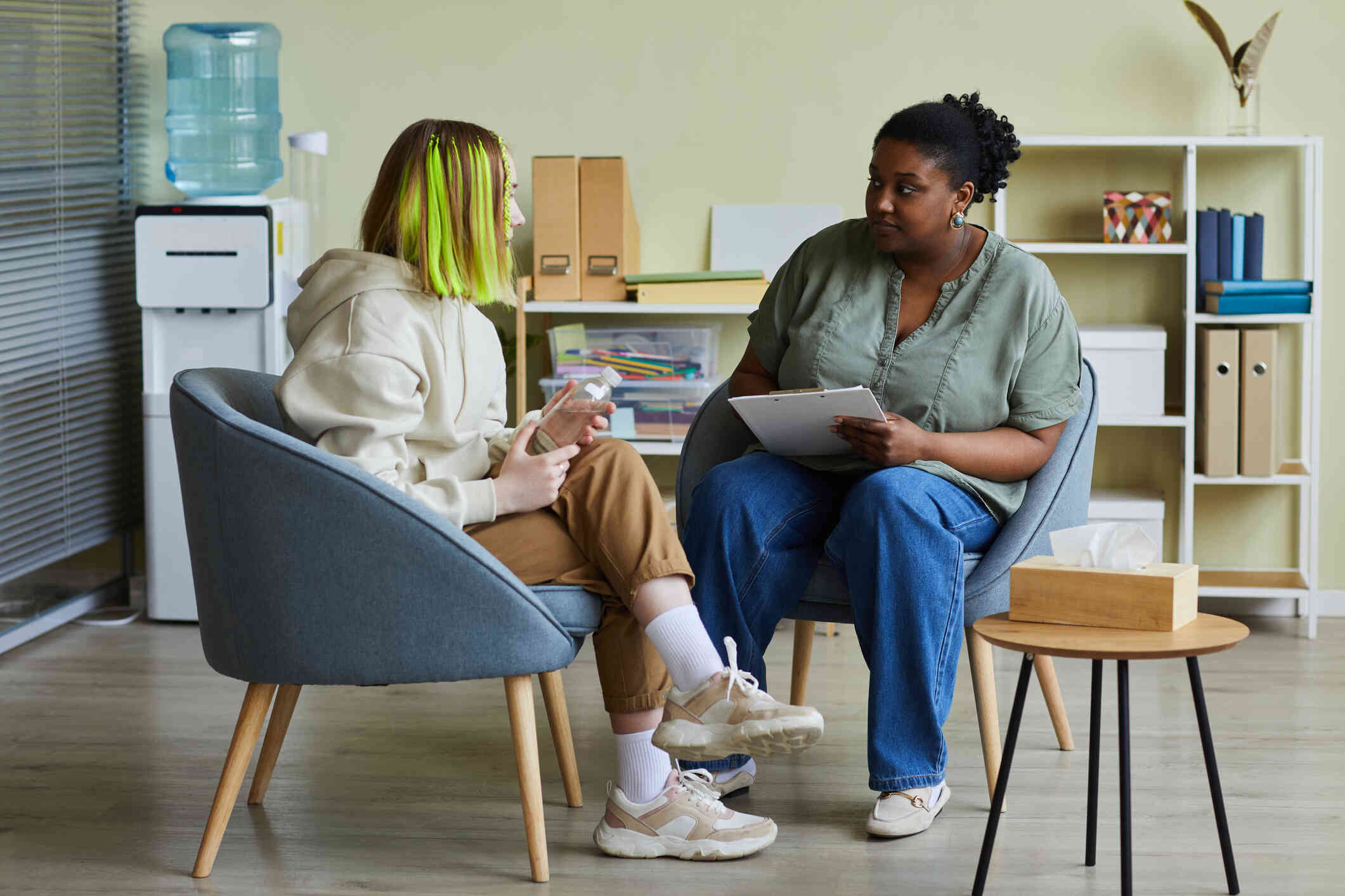 A teenager sits in a chair across from her female therapist and talks.
