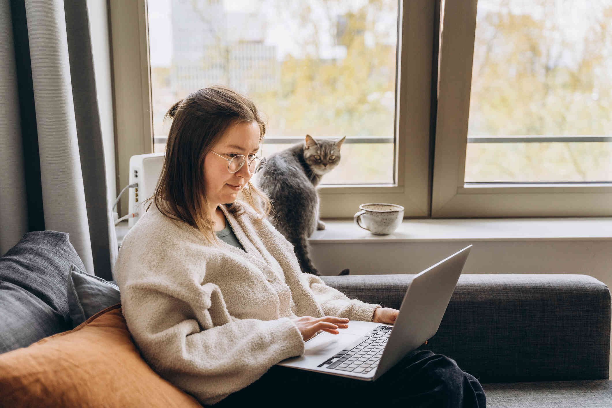 A woman is busy with her laptop, while her cat in the background looks at her.