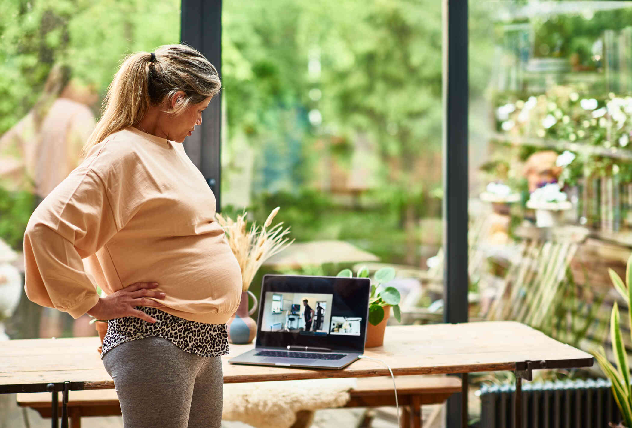 A pregnant woman has a video chat using a laptop on the table infront of her.