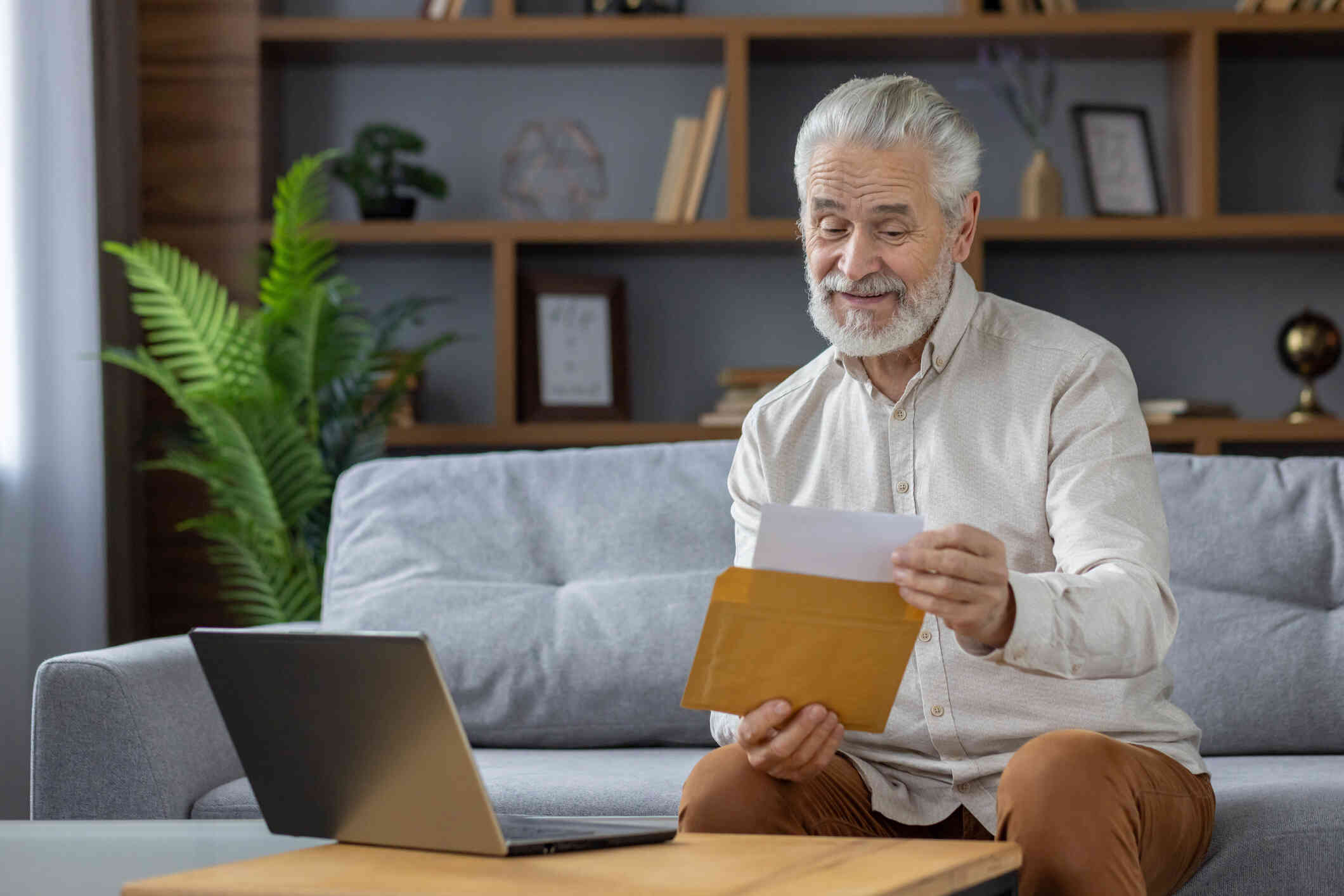 An older man smiles as he shows something to his laptop screen, appearing to be on a video call.