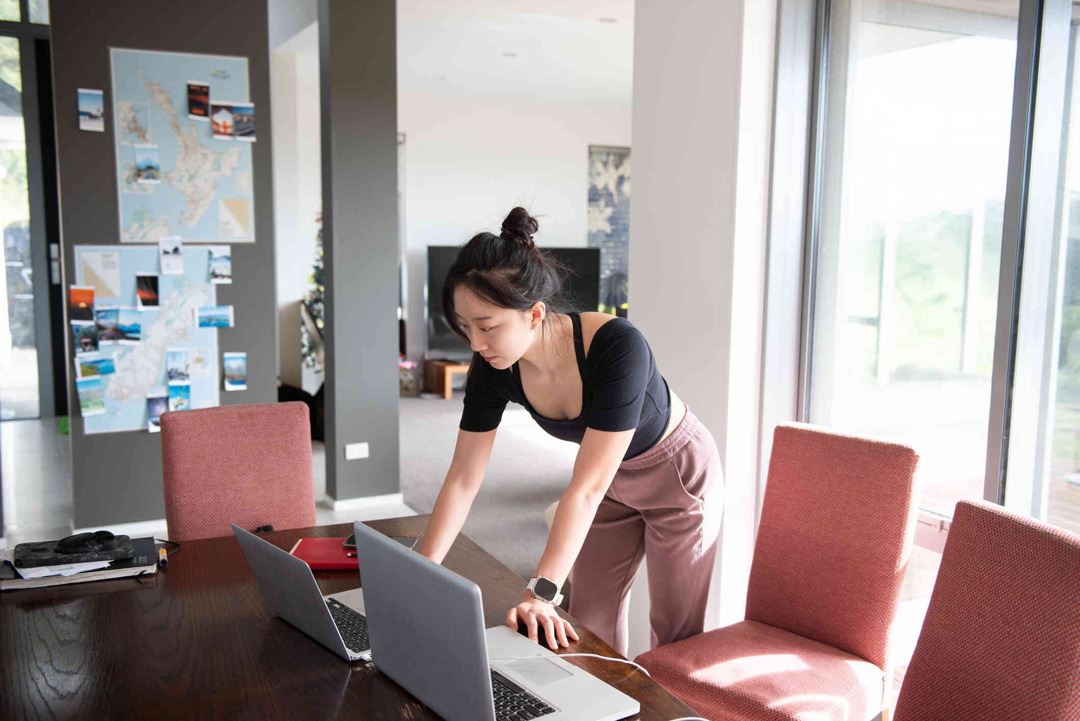 A woman in a black shirt leans over the kitchen table to look at the laptop open infront of her.