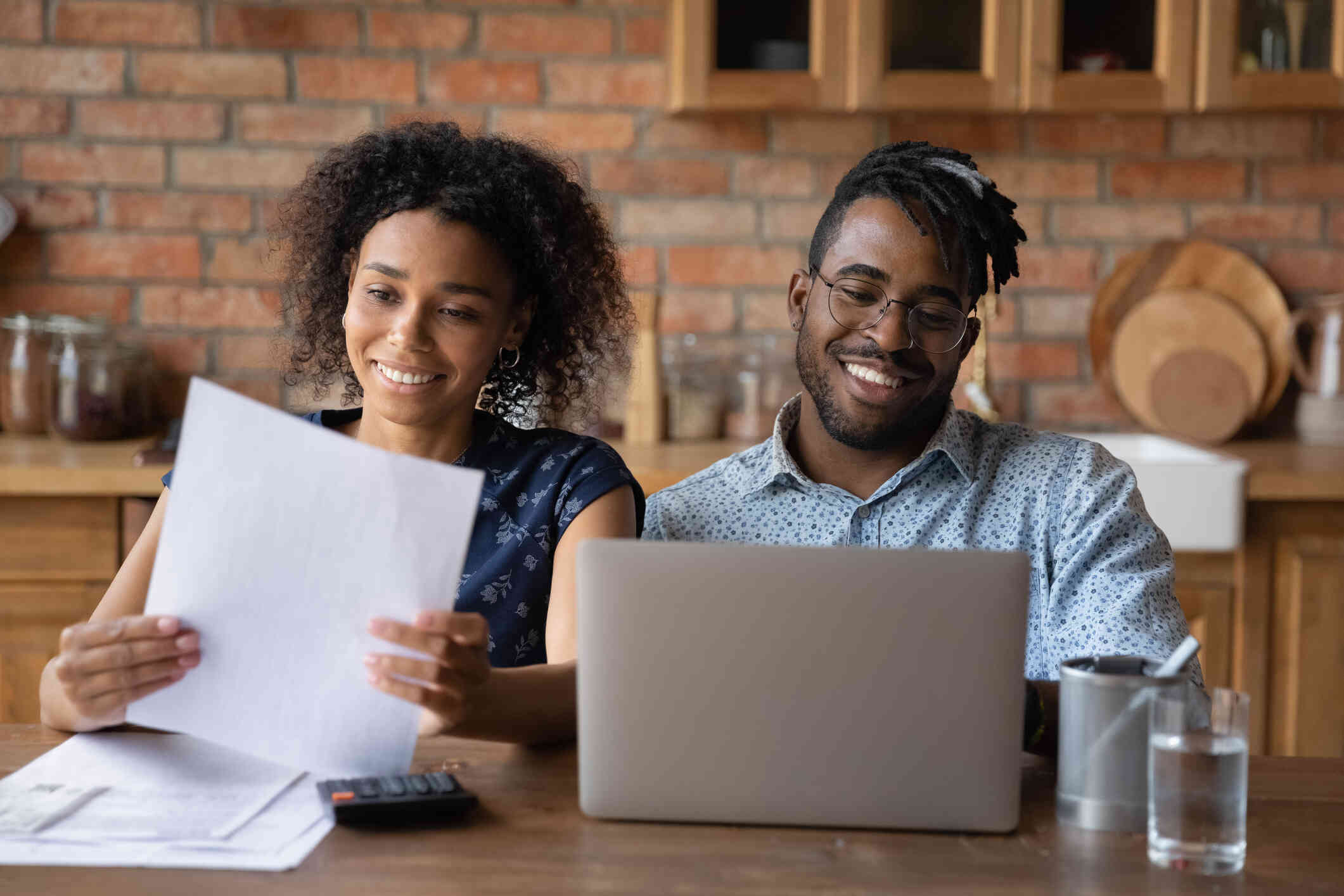 A couple sits at a table, both busy—the woman checking documents while the man focuses on his laptop.