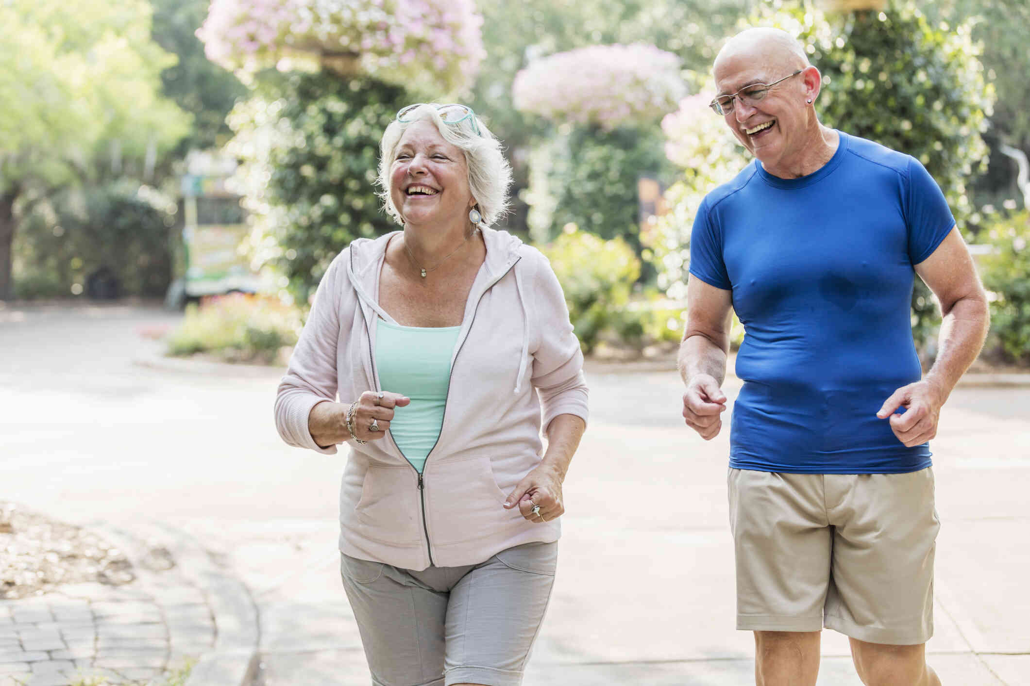 A middle aged man and woman go for a jog together on a sunny day while smiling.