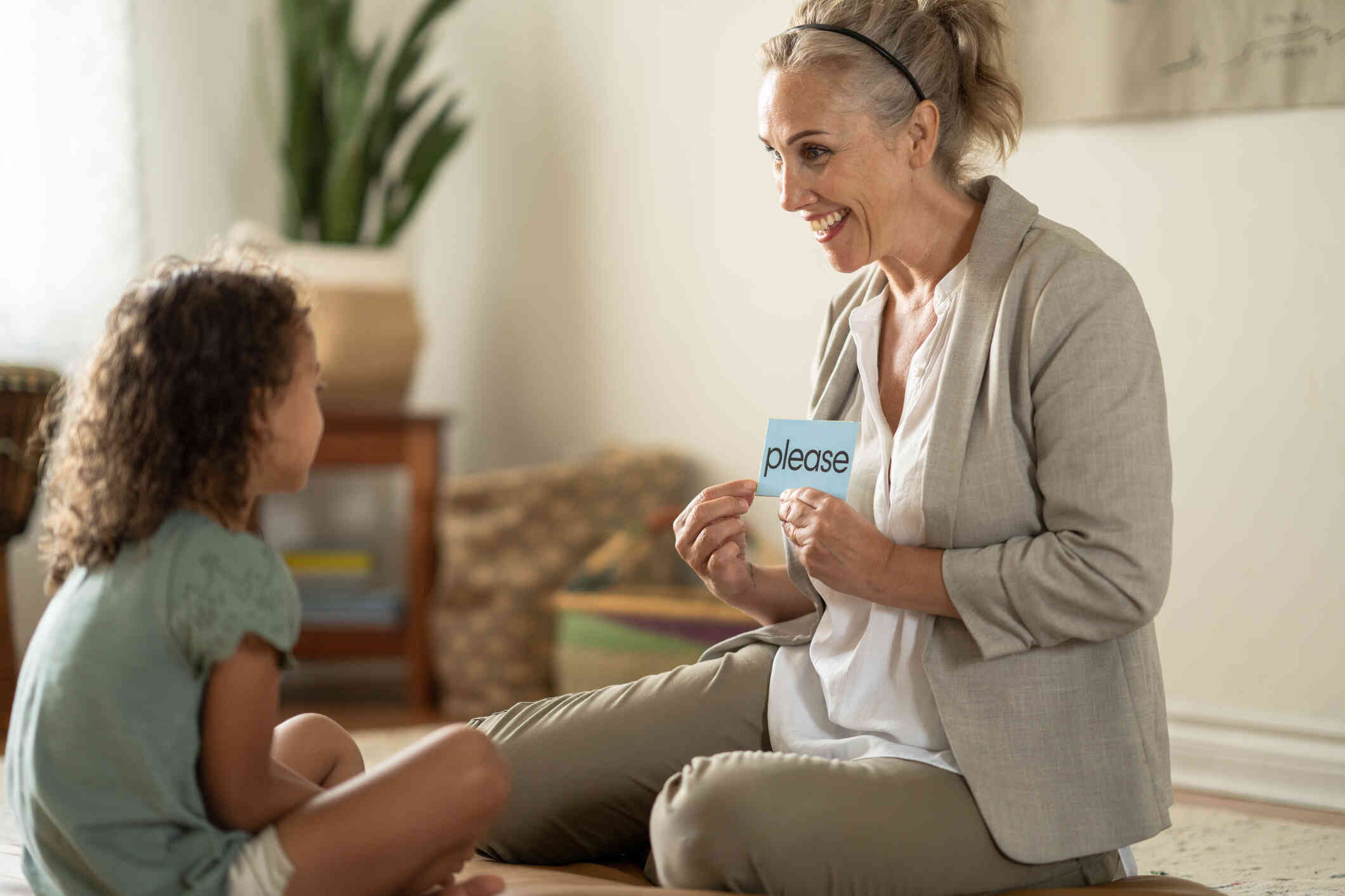 A middle aged female educational psychologist shows a flashcard to the little girl sitting across from her while smiling.