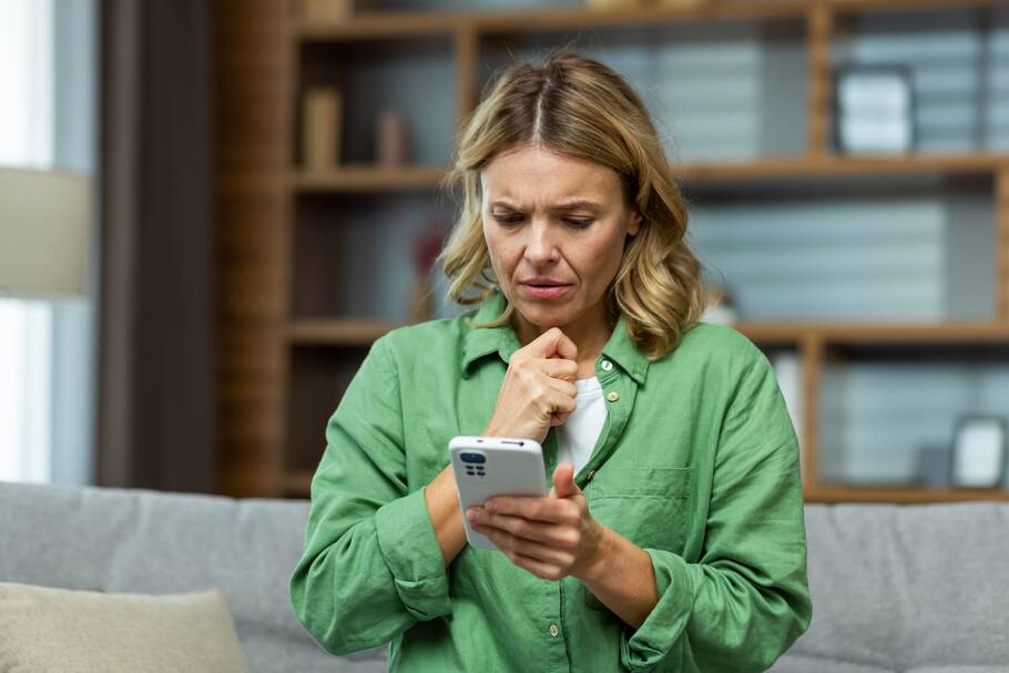 A woman appears stressed as she looks at her phone screen.