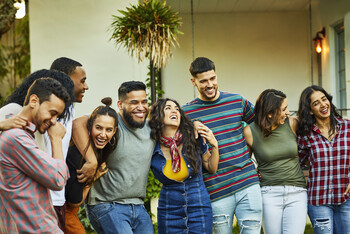 A group of men and women stand outside with their arms around each other and smile.