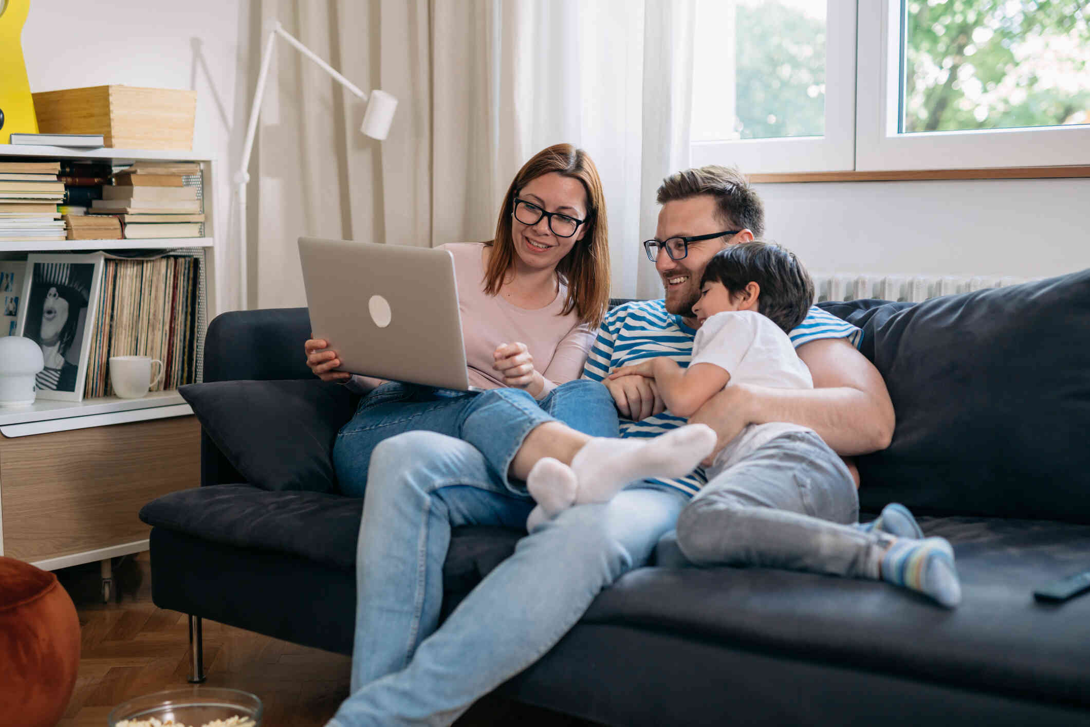 A family seated comfortably on their couch engages in a video call, smiling warmly at their laptop screen.