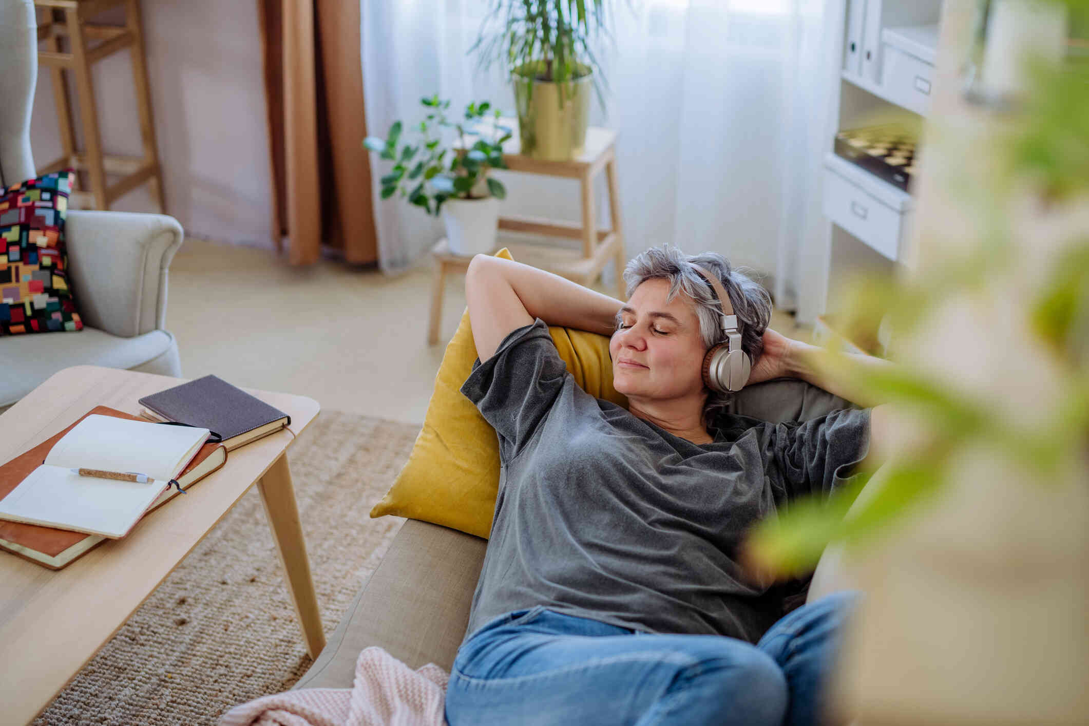 A woman wearing headphones smiles slightly as she lays on her back on a couch and closes her eyes.