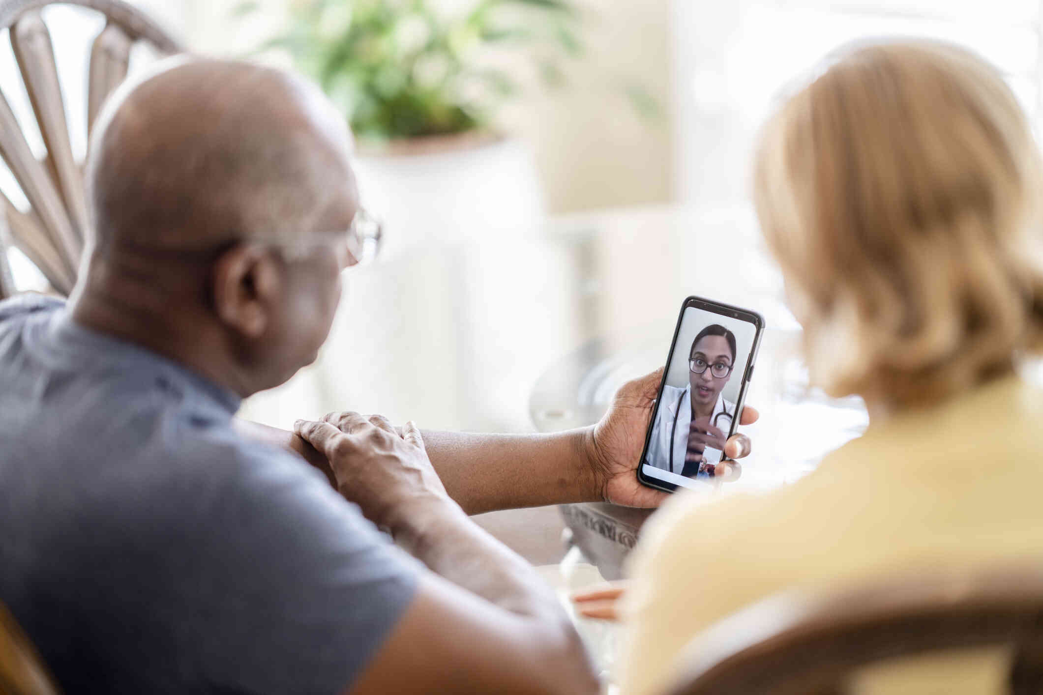 An elderly couple seated together, participating in a therapy session via their phone.