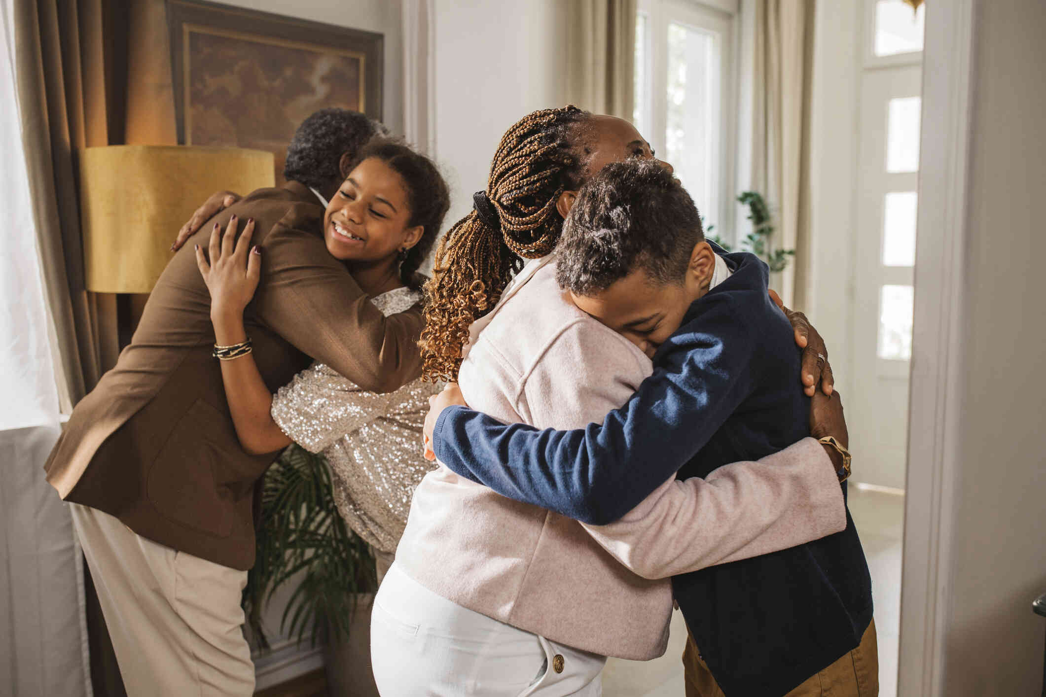 A mother and father hug their children while standing in their home and smiling.