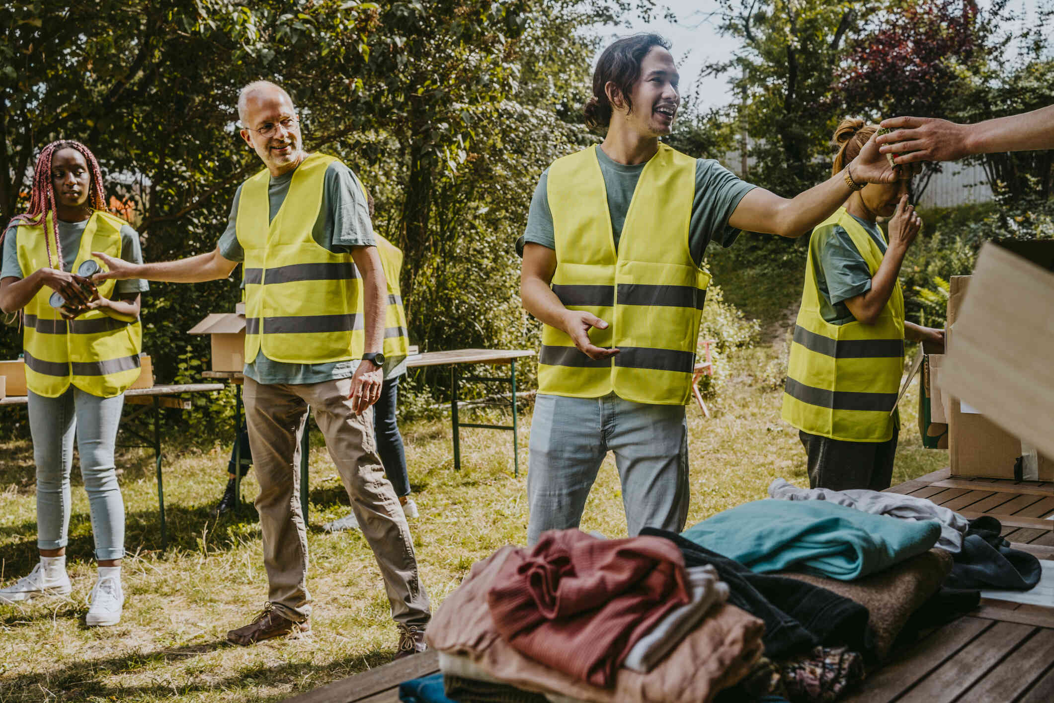 Three people in yellow safety vests smile as they stand outside near folding tables and organize donations.