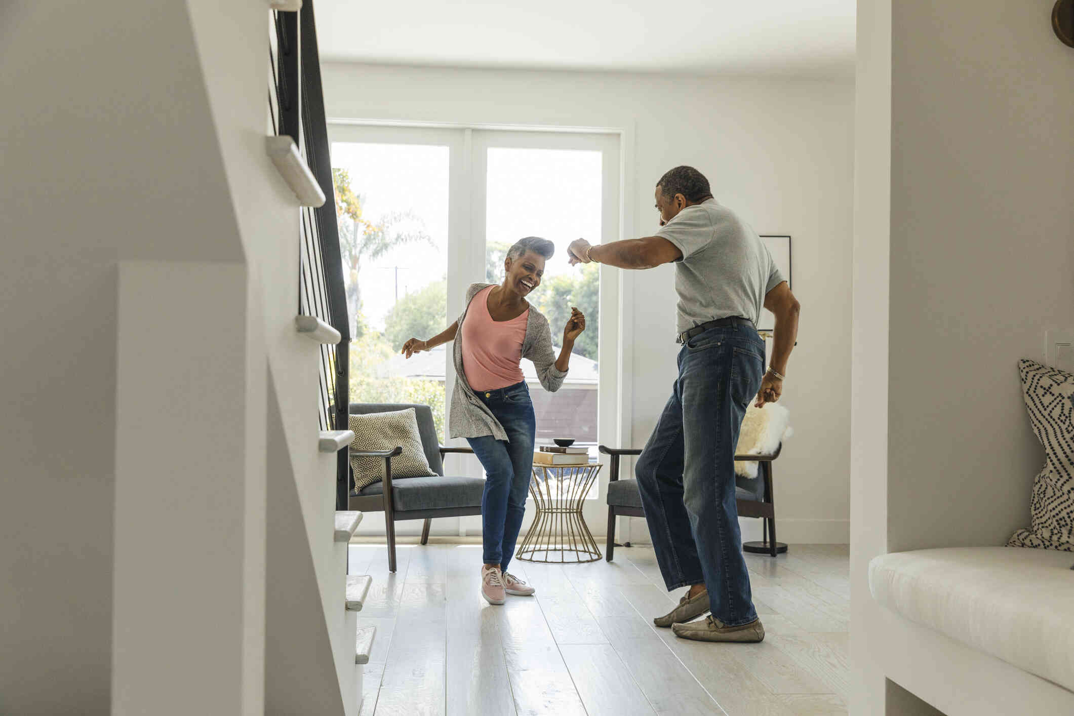 Amature male and female couple dance playfully in the living room while smiling.