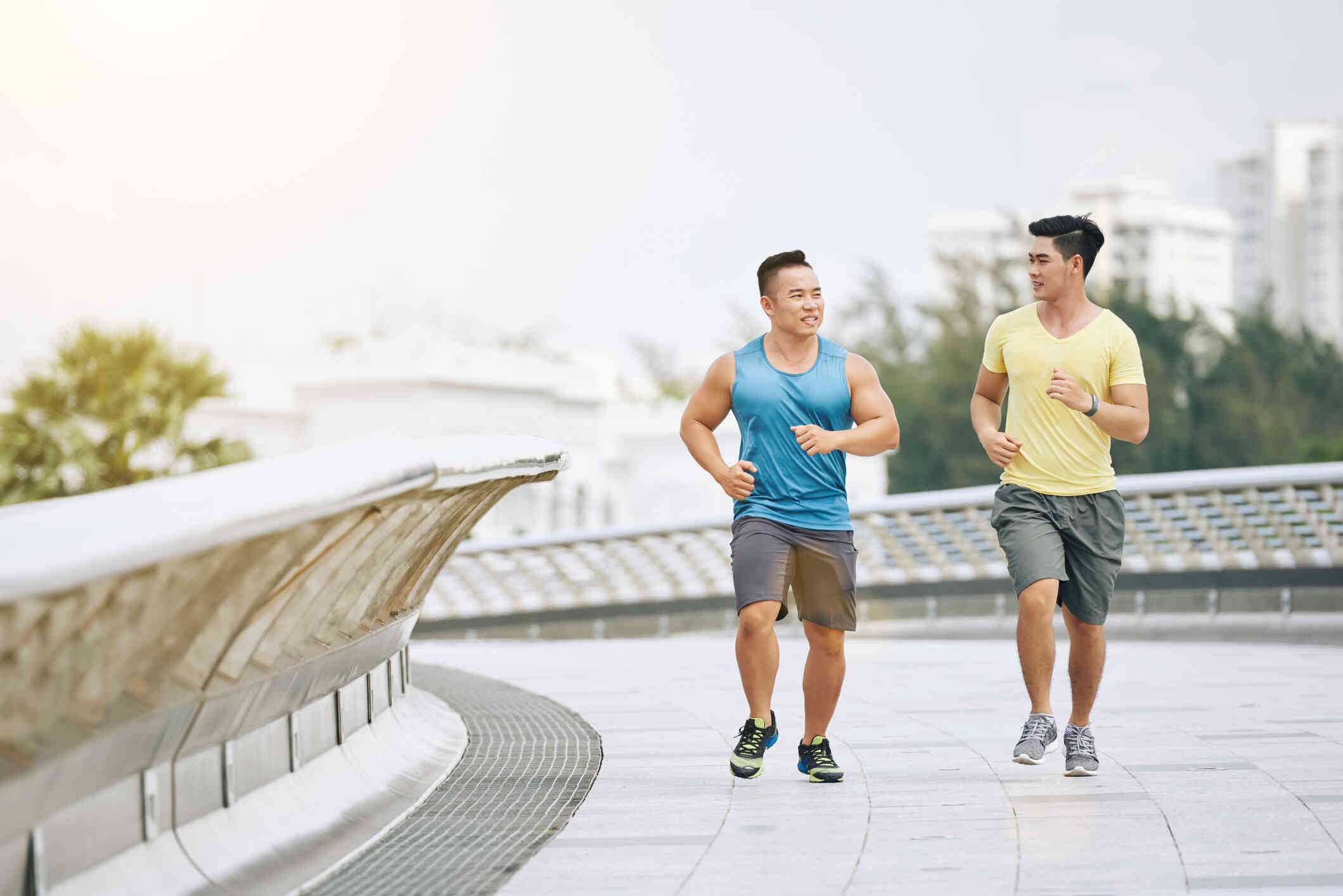 Two male athletes in workout clothes go for a run on a bridge on a sunny day.