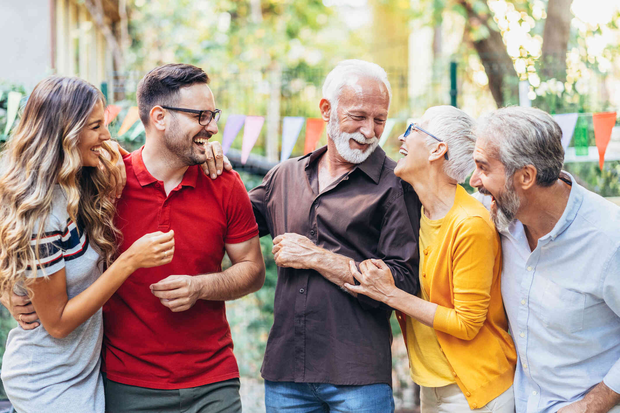 A group of adults stand outside on a sunny day while smiling and laughing.