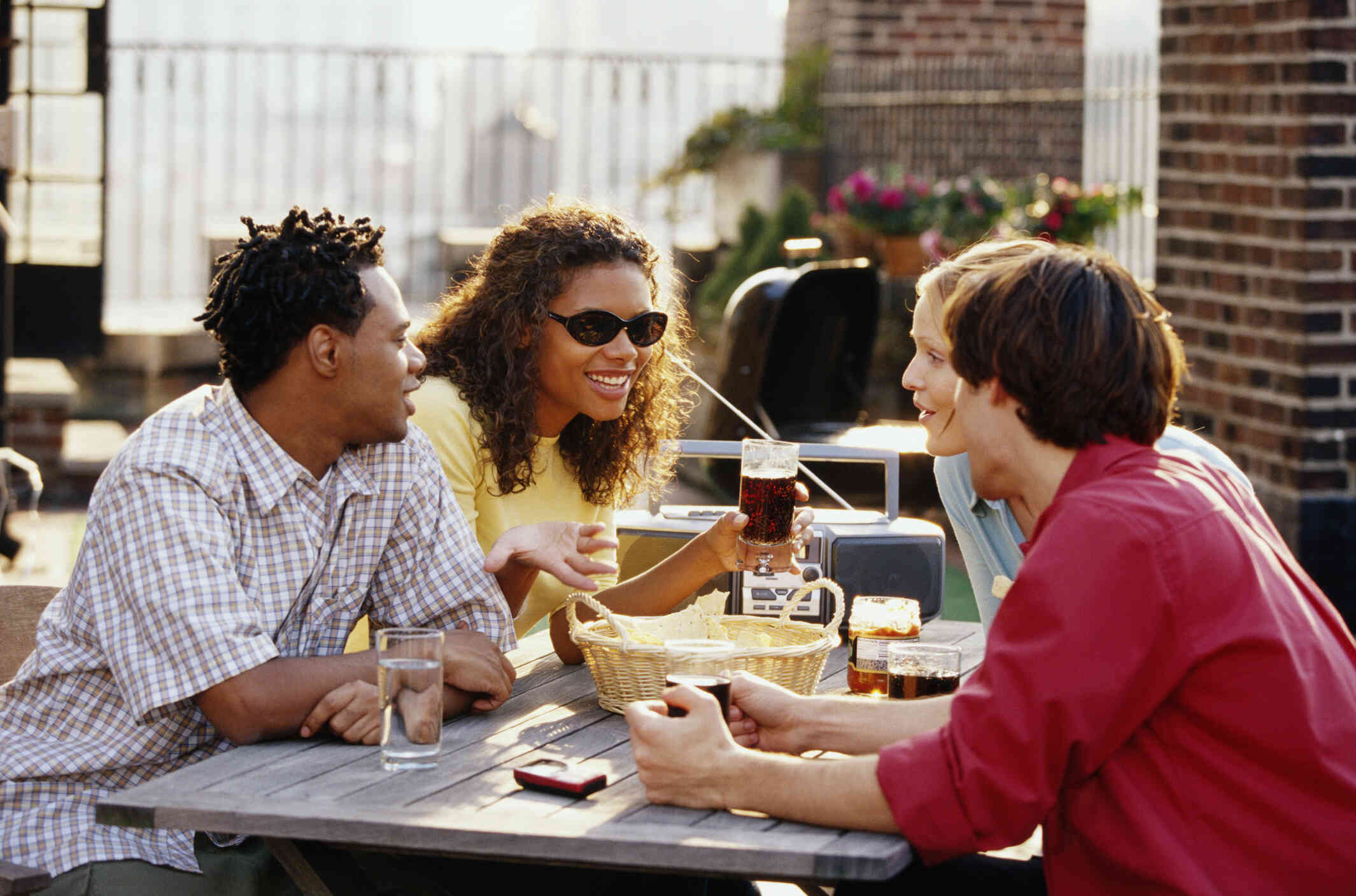 A group of adult friends sit at a restaurant table outside on a patio on a sunny day.