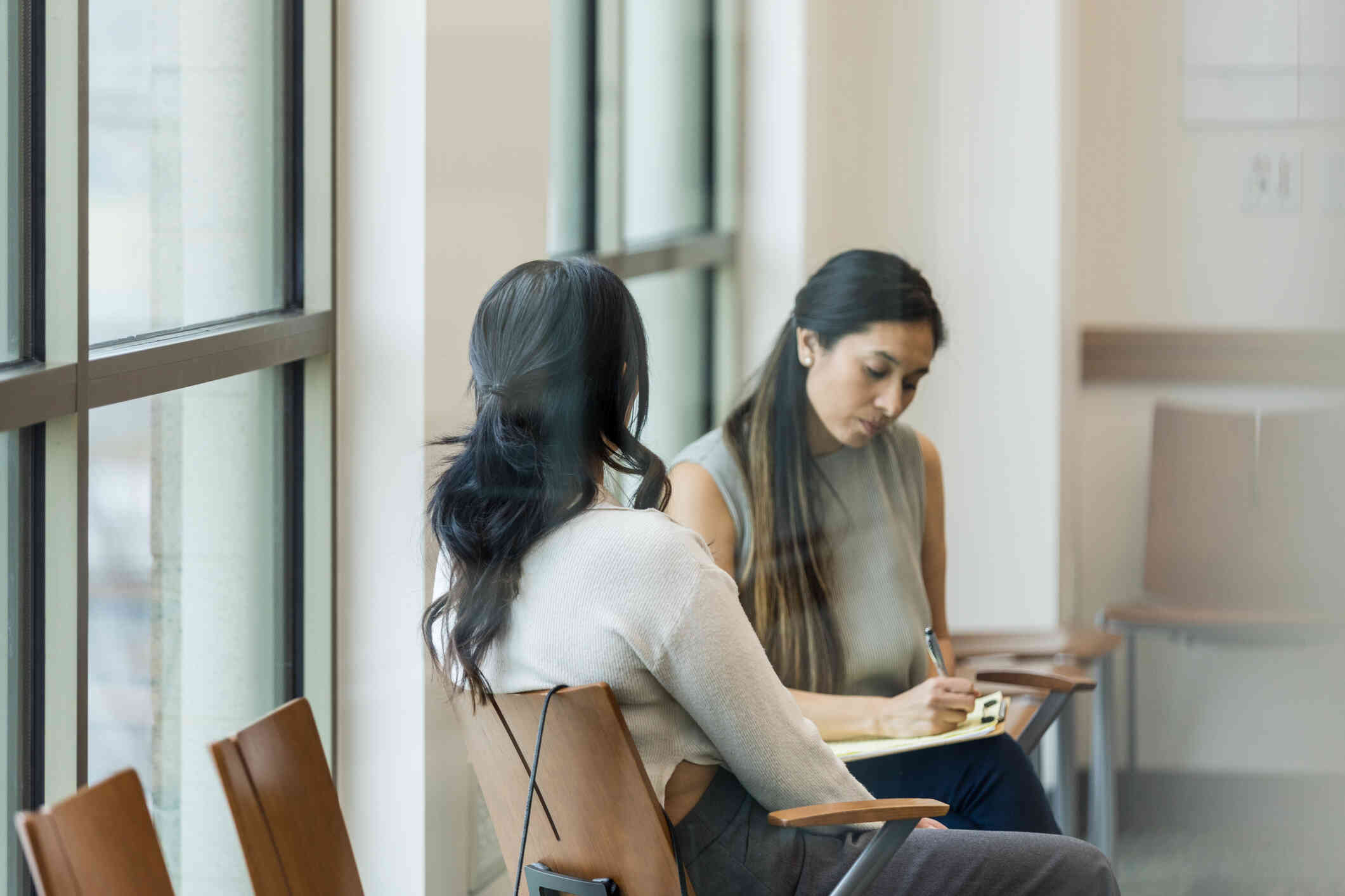 A female therapist writes in a notepad while sitting across from her female patient during a therapy session.