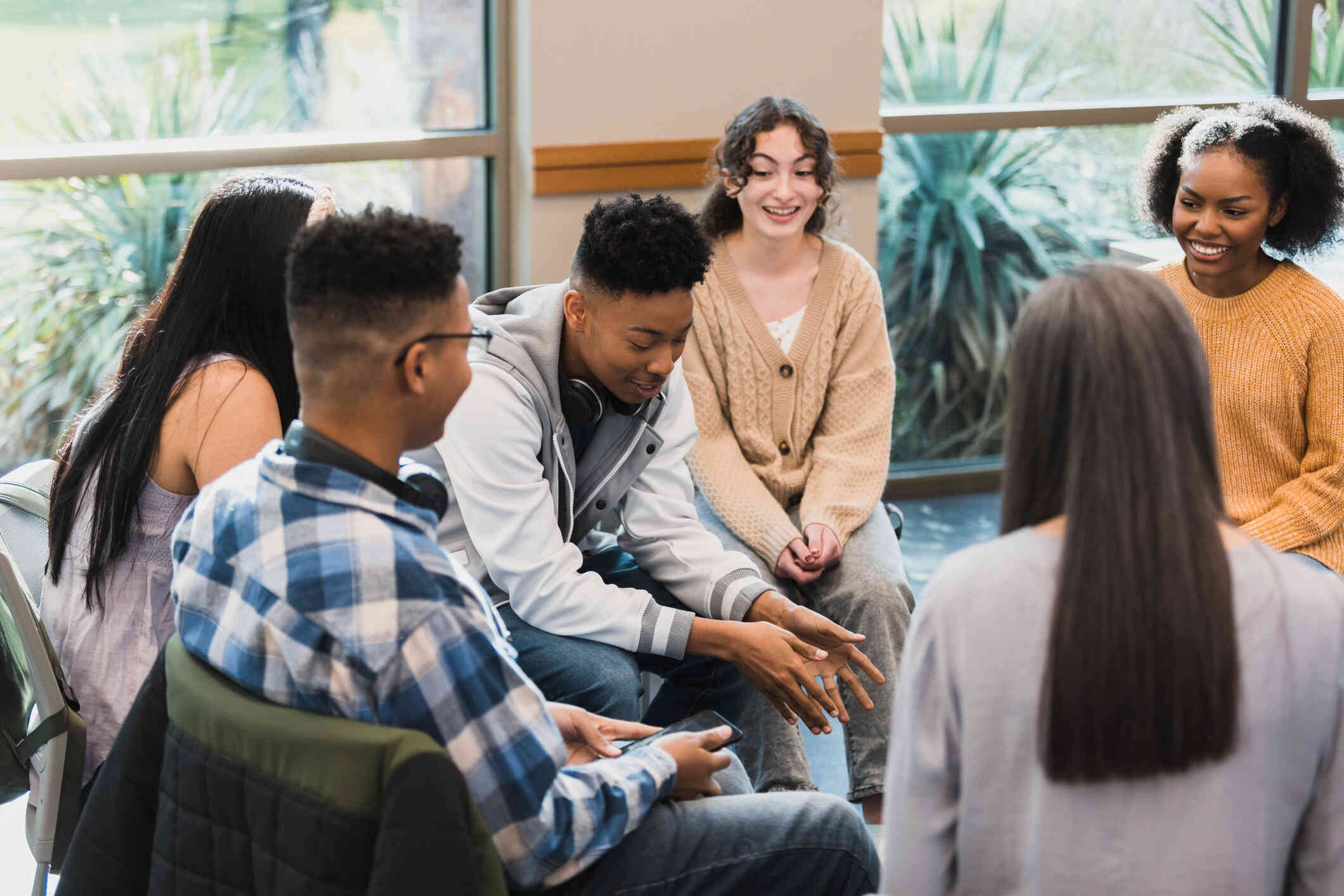 A group of teenagers sit together in a group therapy circle and have a conversation.