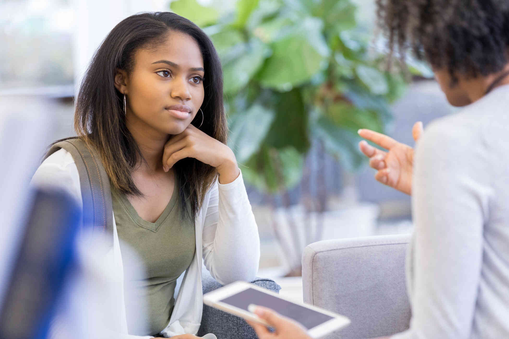 A girl in a green shirt sits across from her female therapist and listens as the therapist talks.