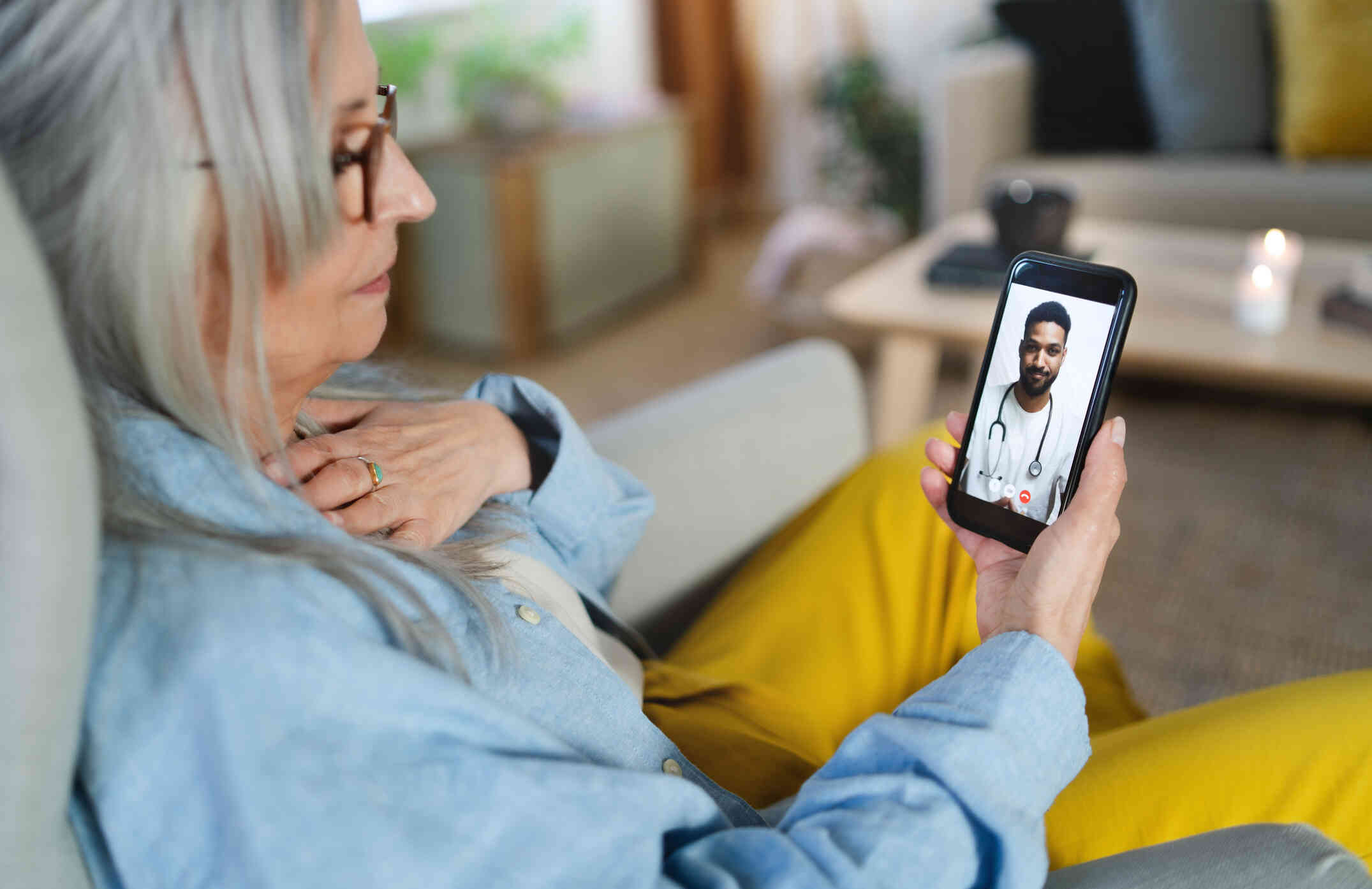 A middle aged woman looks down at the cellphone on her hand while talking to a male doctor during a telehealth video call.