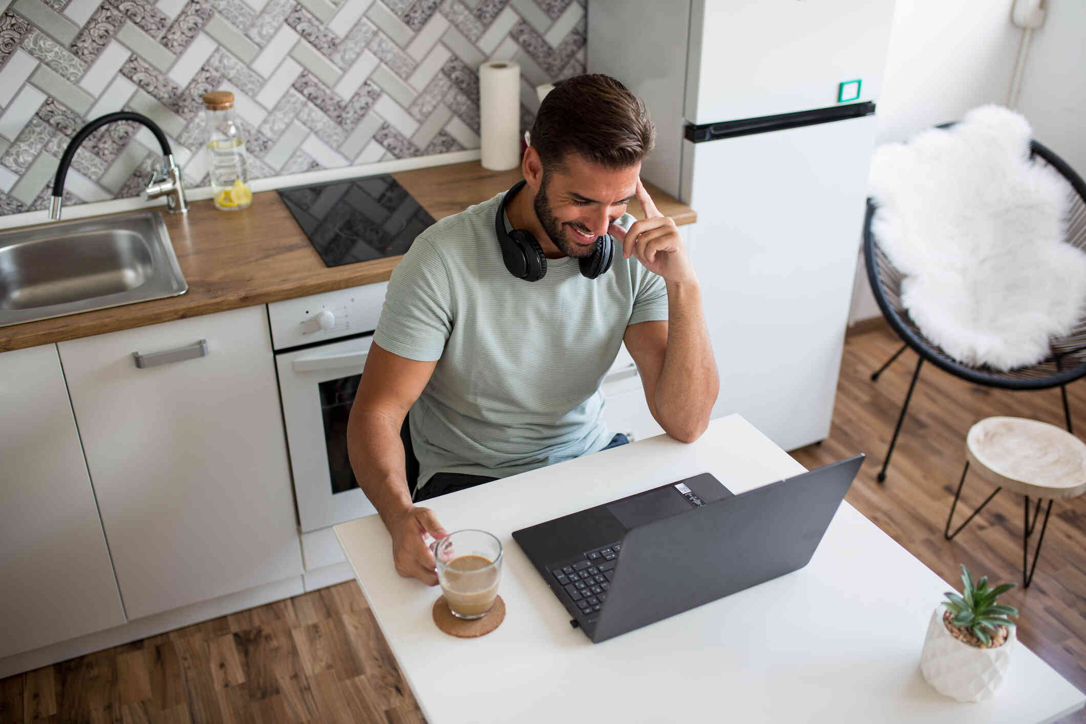 A man sitting at his kitchen table while holding a coffee is attending an online call.