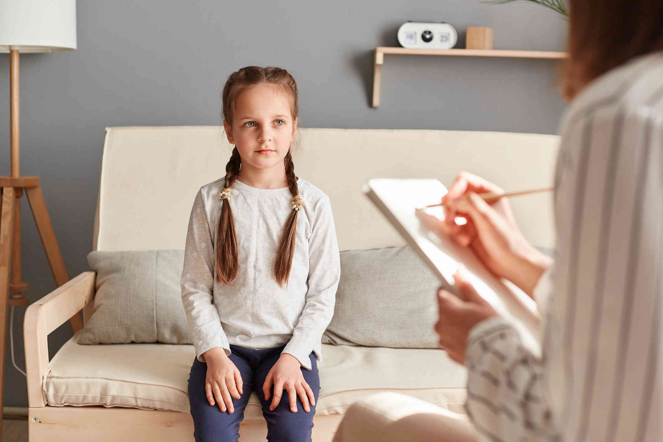 A little girl with pigtails sits on a couch across from her therapist.