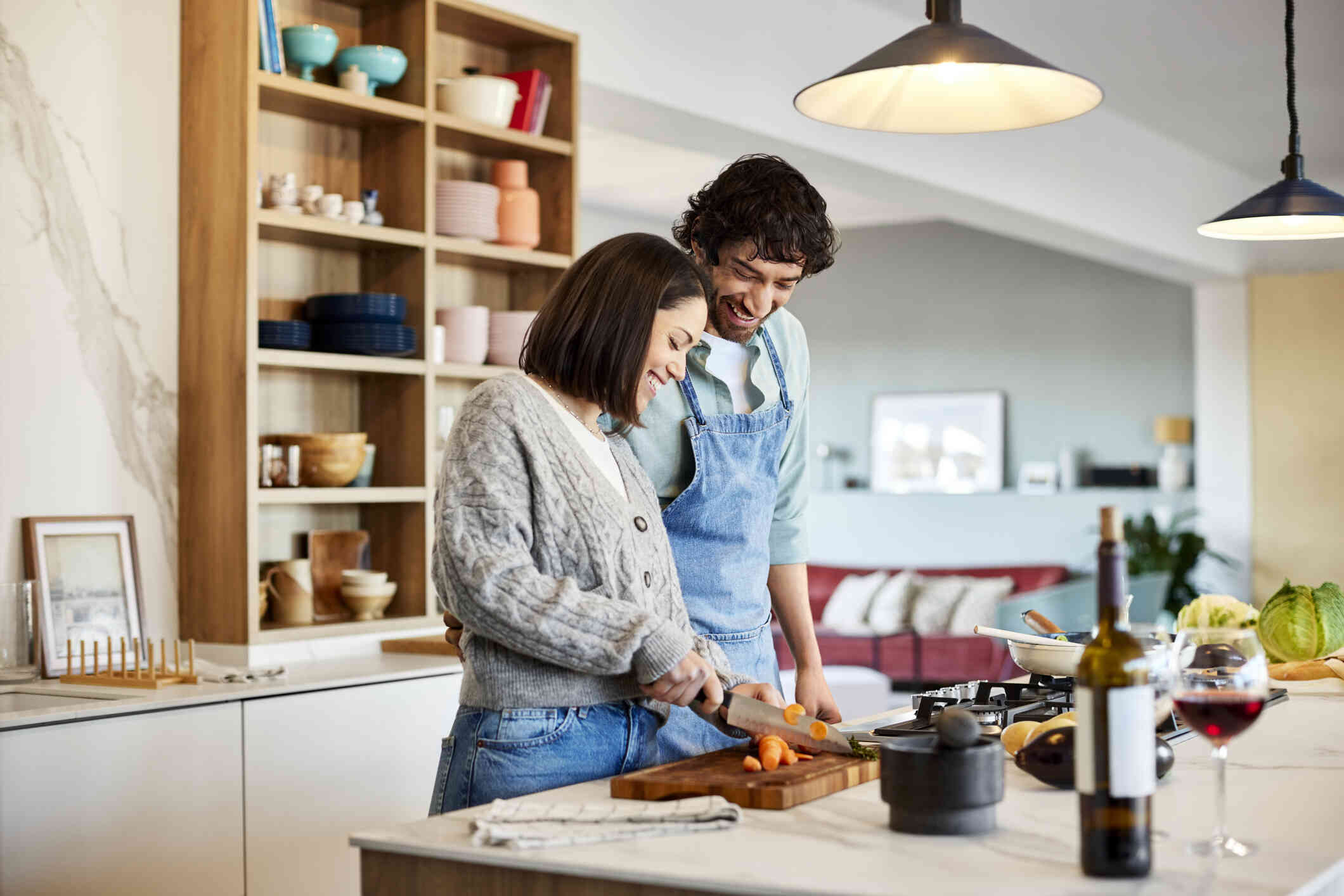A male and female couple stand side by side in the kitchen and cook dinner together while smiling.