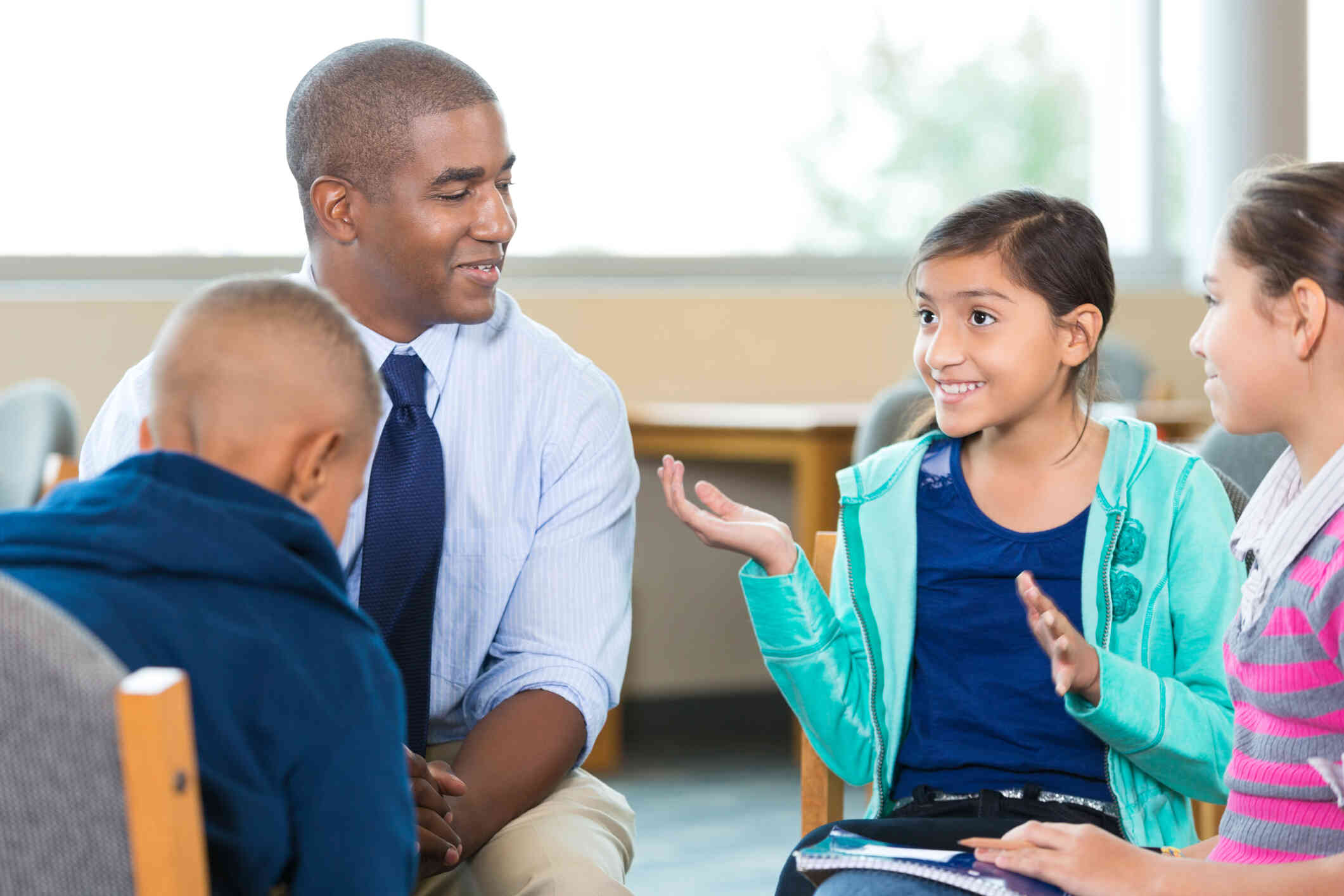 A young man sitting in a circle with 3 kids in a school.