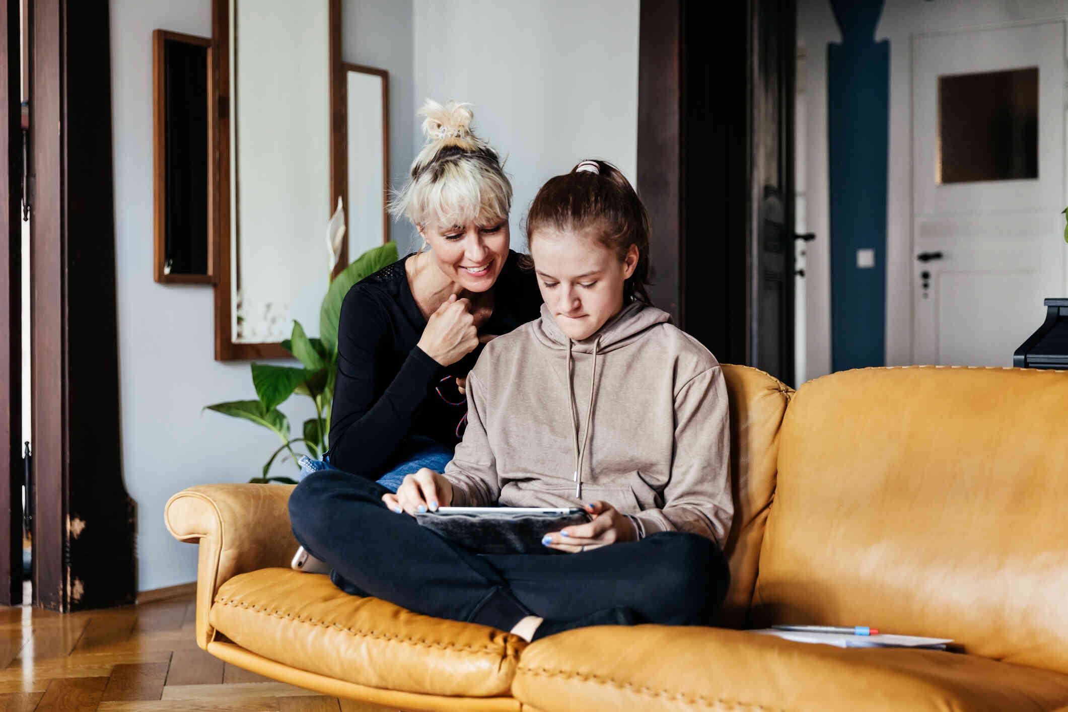 A young girl with a nervous expression and her mother sit on her couch as they both look down at the computer 