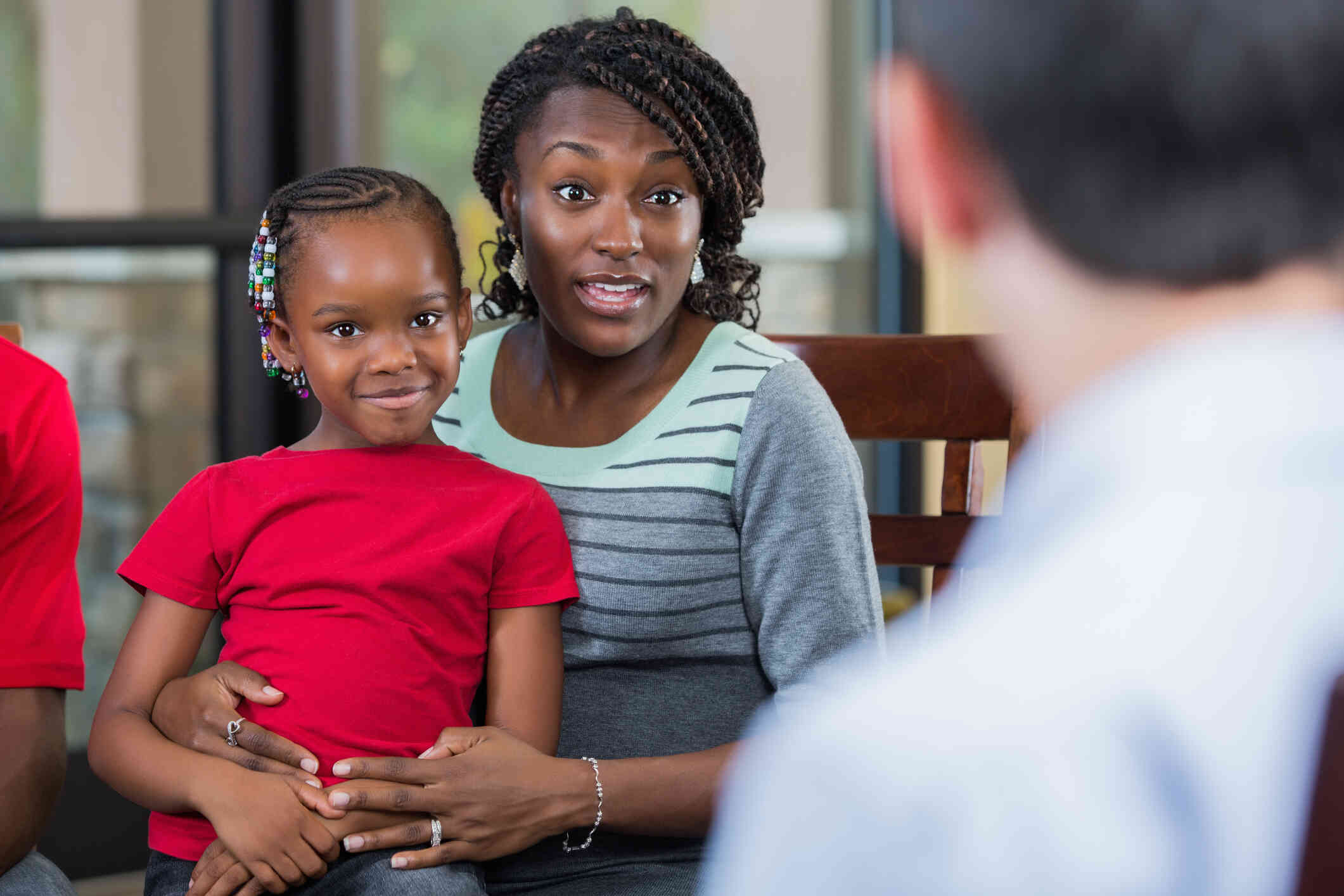 A young girl sits on her mothers lap as the mother talks to the therapist sitting across from them.