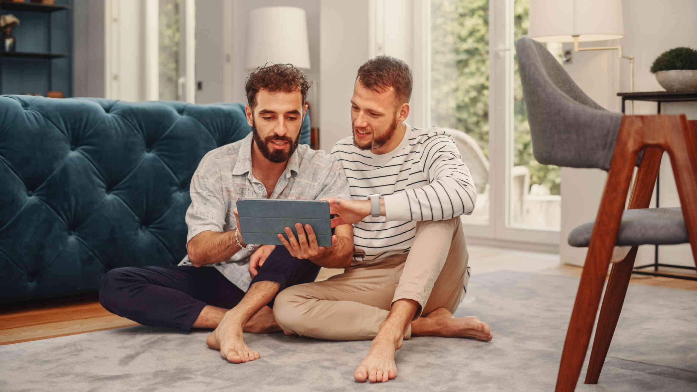 A couple seated on the floor, both looking at a tablet.