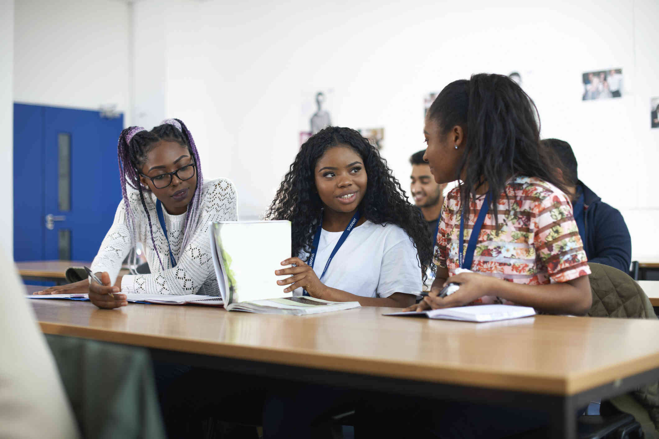 A group of college students sit at tables in a classroom while talking.