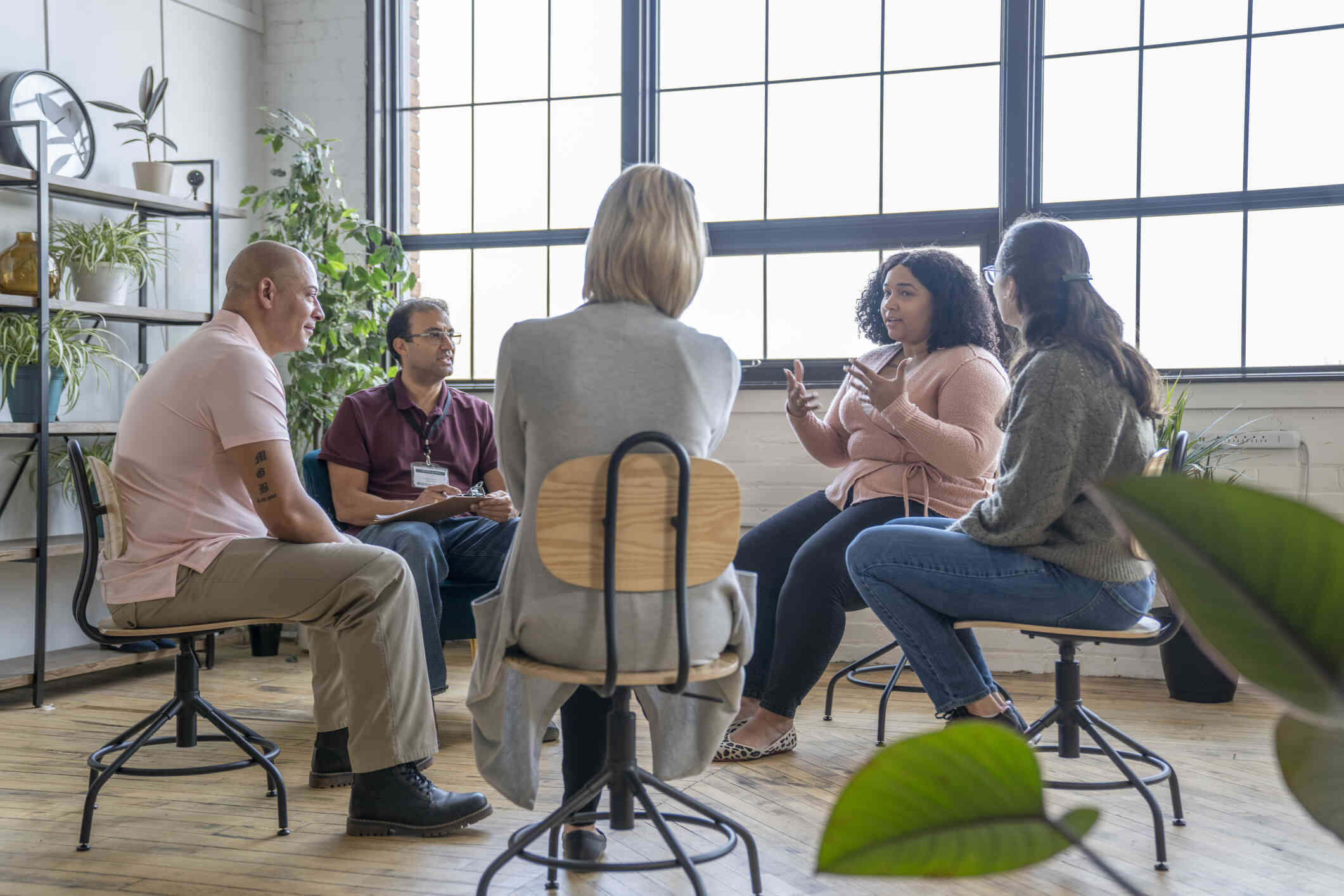 A group of adults sit in chairs in a circle and talk during a support group meeting.