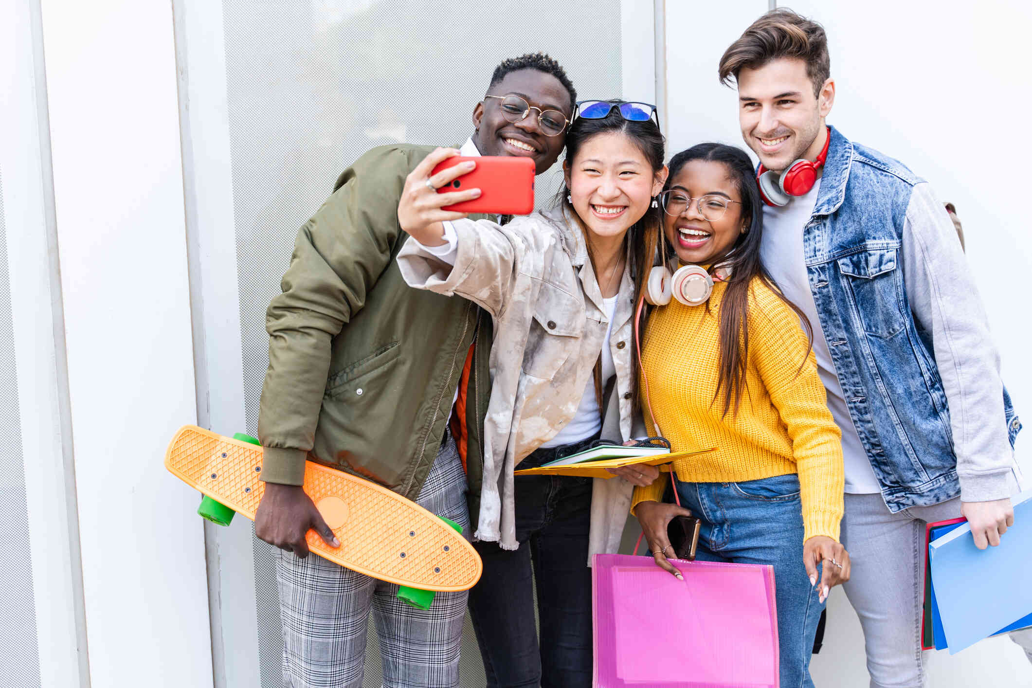 A group of four teenagers stand outside and gather together to take a selfie while smiling.