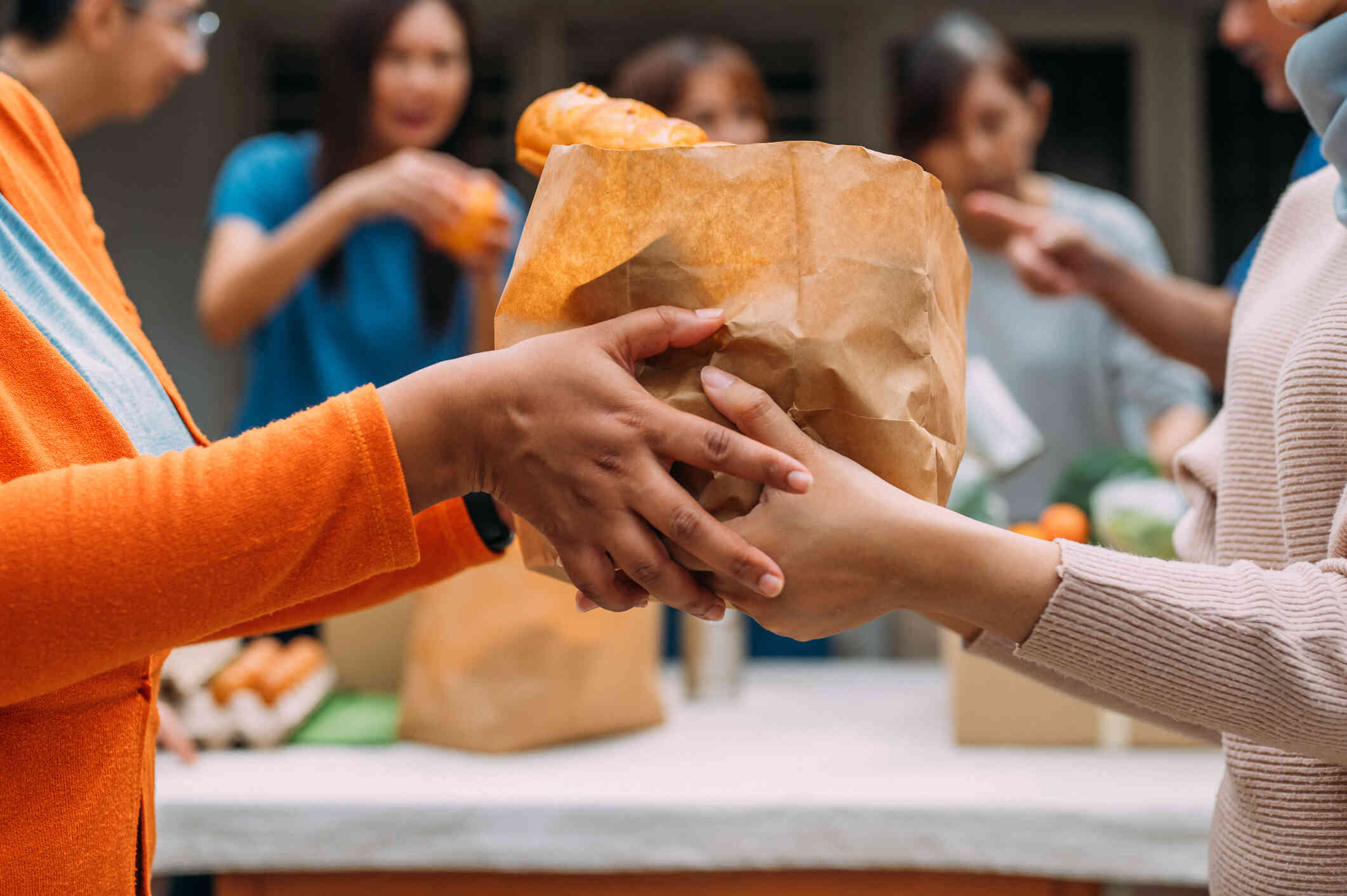 A close up of two people passing around a brown paper bag fill of food while volunteering.