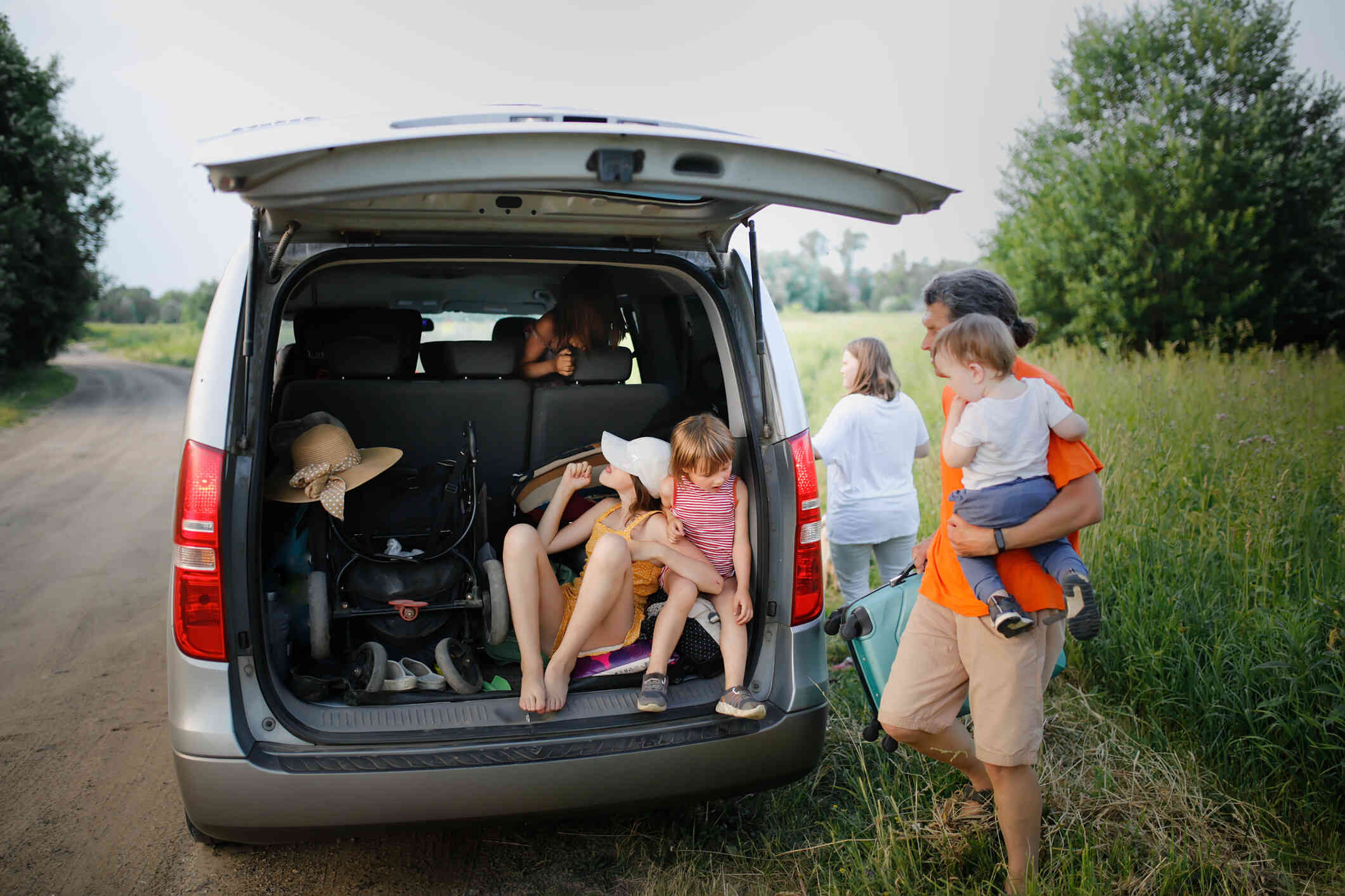 A family gathers together in and around a minivan while parked in an open field on a sunny day.