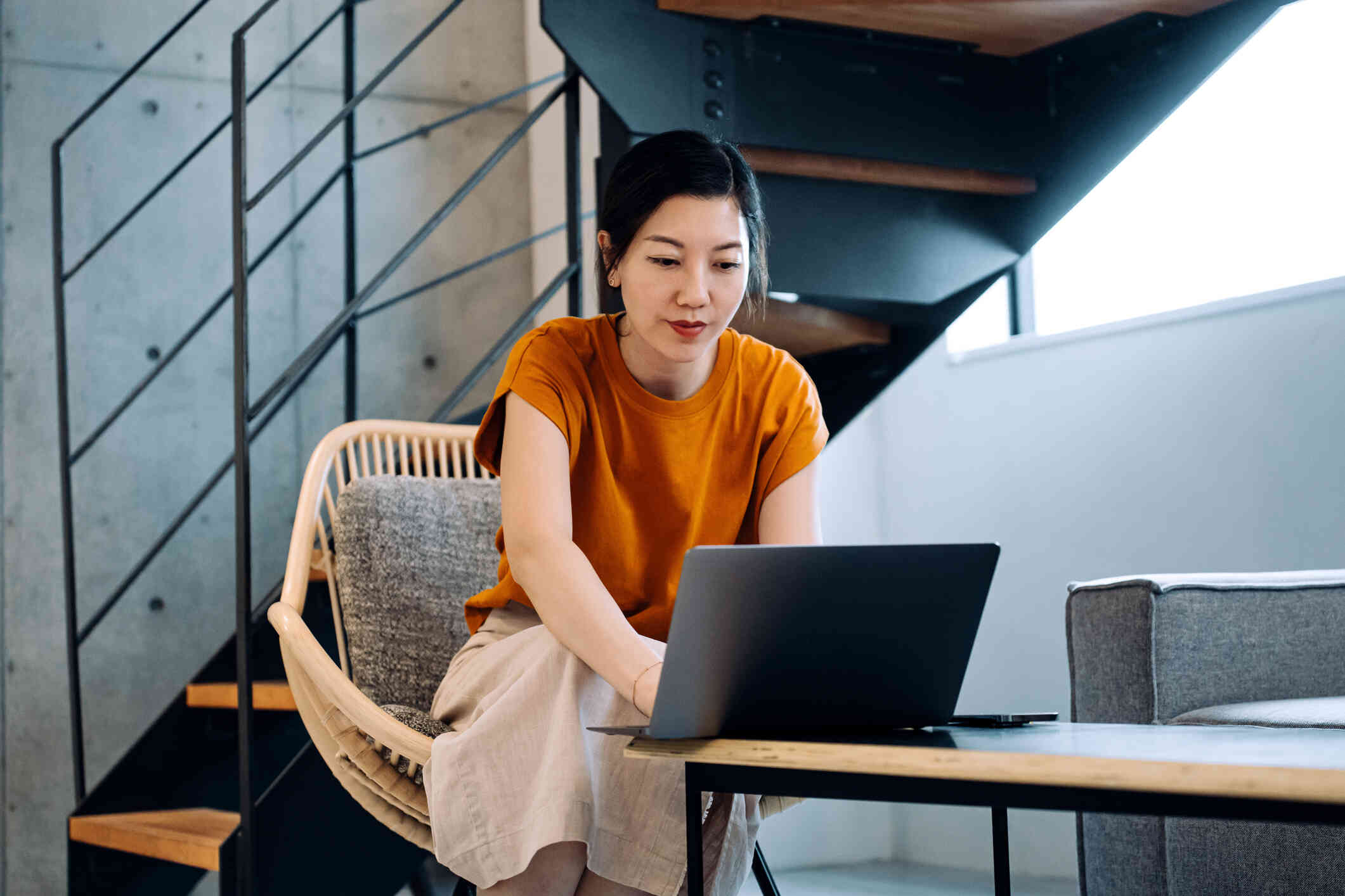 A woman in a yellow shirt sits at her desk with her laptop open infront of her and gazes off while deep in thought.