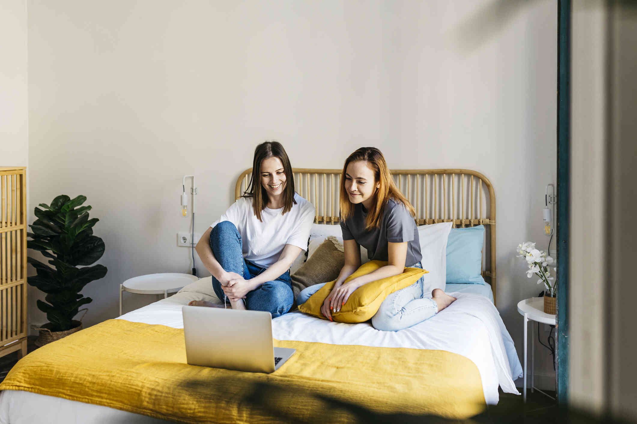 Two women are sitting at their bed laughing with and talking to each other.