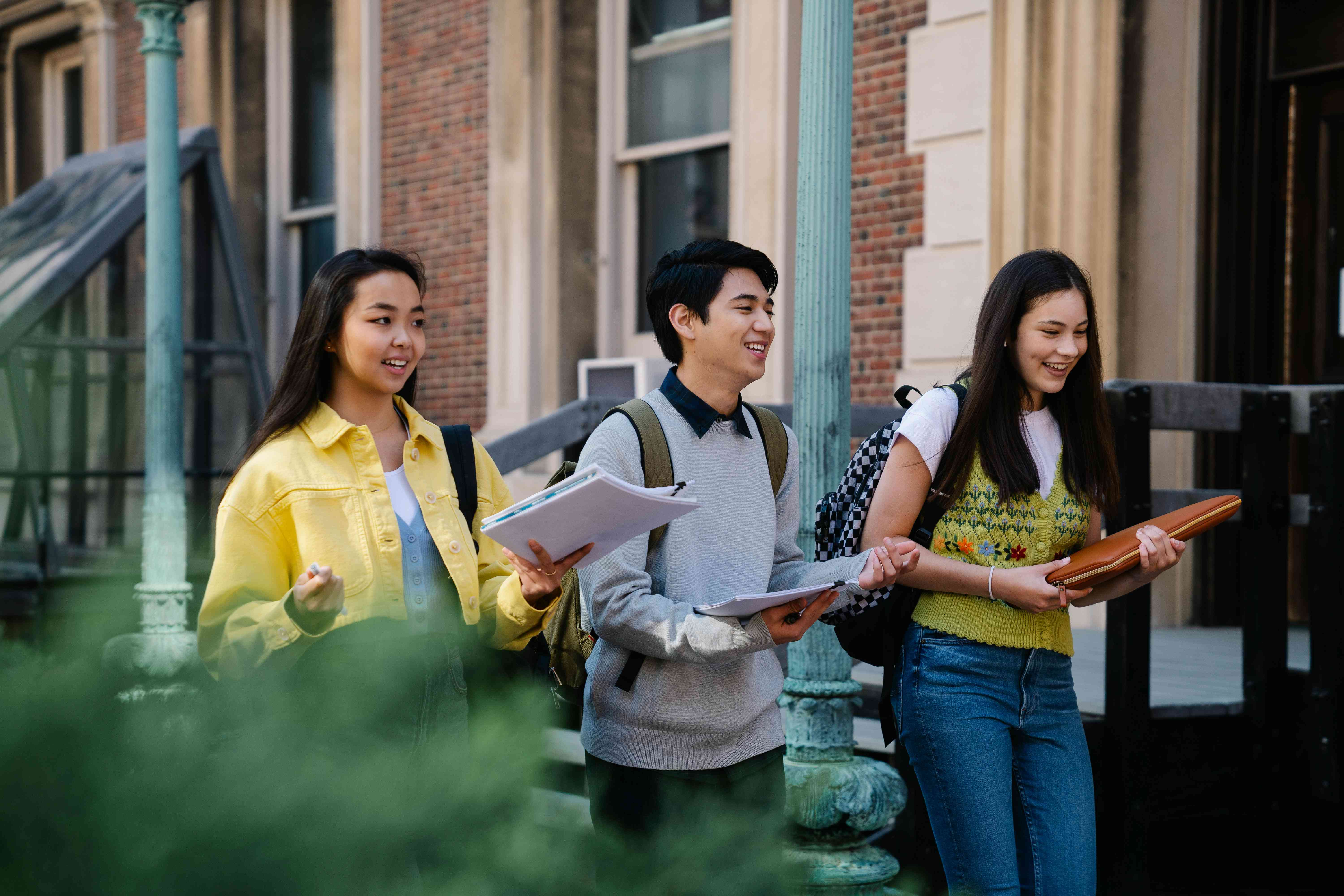 A group of friends walk down a sidewalk near a road on a fall day while laughing and talking