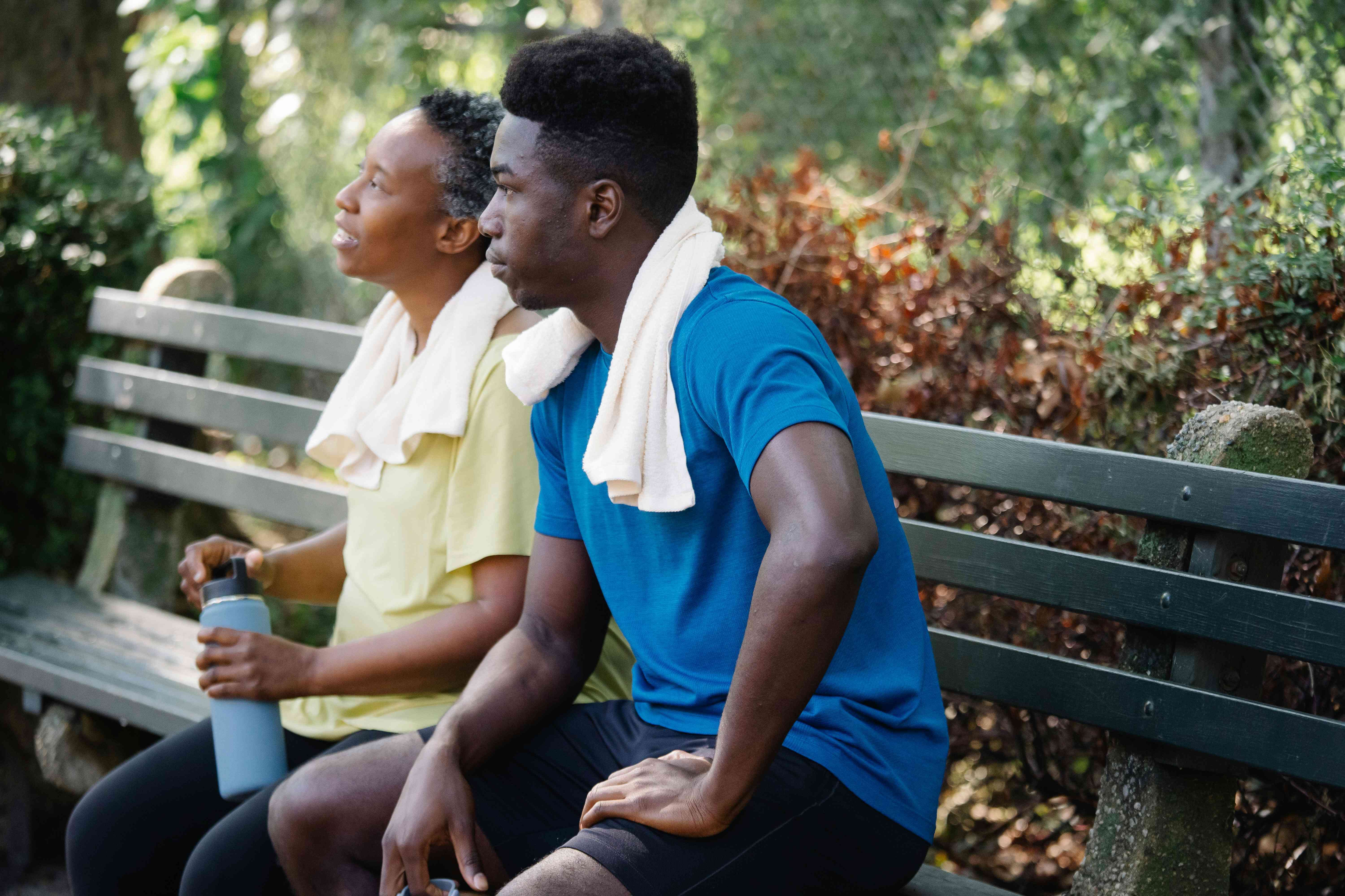 A woman in workout clothes sits on a bech next to a man as they smile and talk with one another.